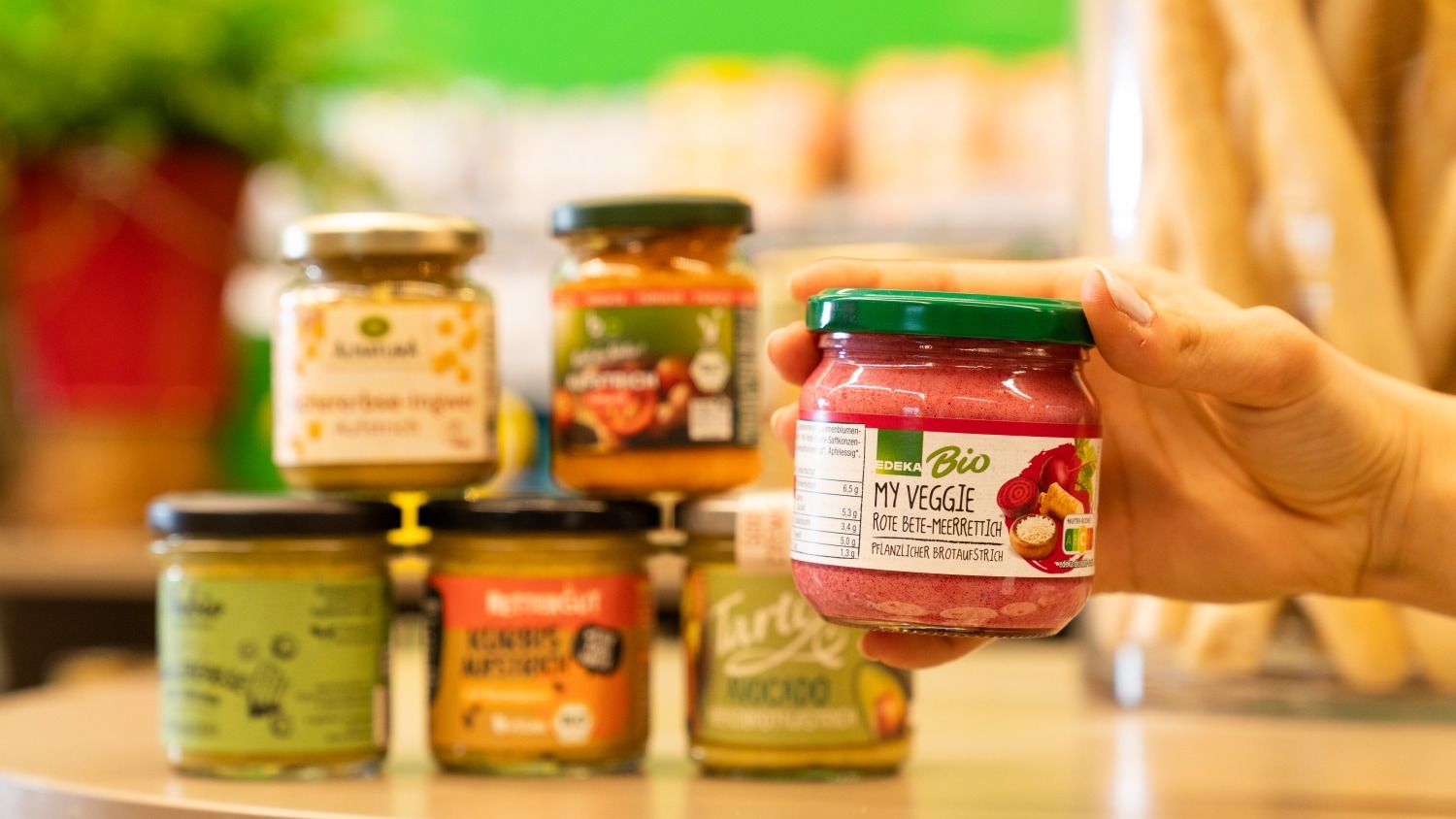 Nahaufnahme einer Hand die ein Glas Bio-Aufstrich von EDEKA hält. Im Hintergrund sind unscharf weitere Gläser zu erkennen.