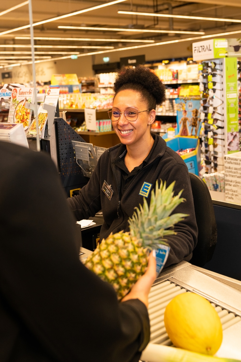 Eine lächelnde Mitarbeiterin sitzt an der Kasse eines EDEKA-Marktes.
