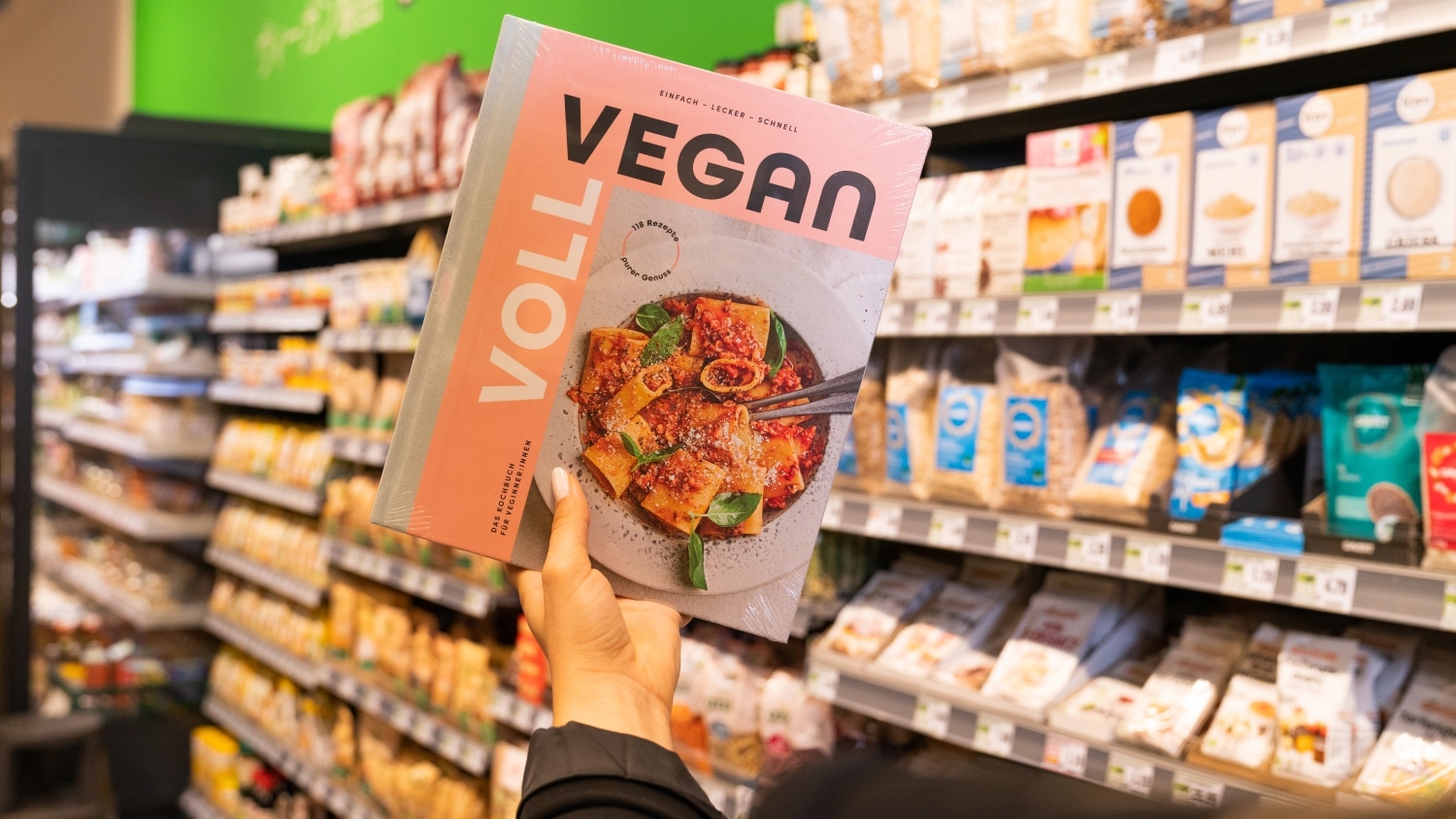 Eine Hand hält ein veganes Kochbuch.