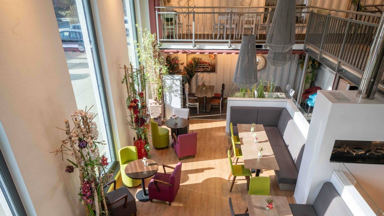 Blick von der Balustrade eines Cafés in dessen lichtdurchfluteten Innenraum.