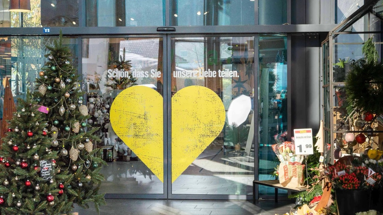 Nahaufnahme der Eingangstüren eines Edeka-Marktes, die mit einem großen gelben Herz bedruckt sind.