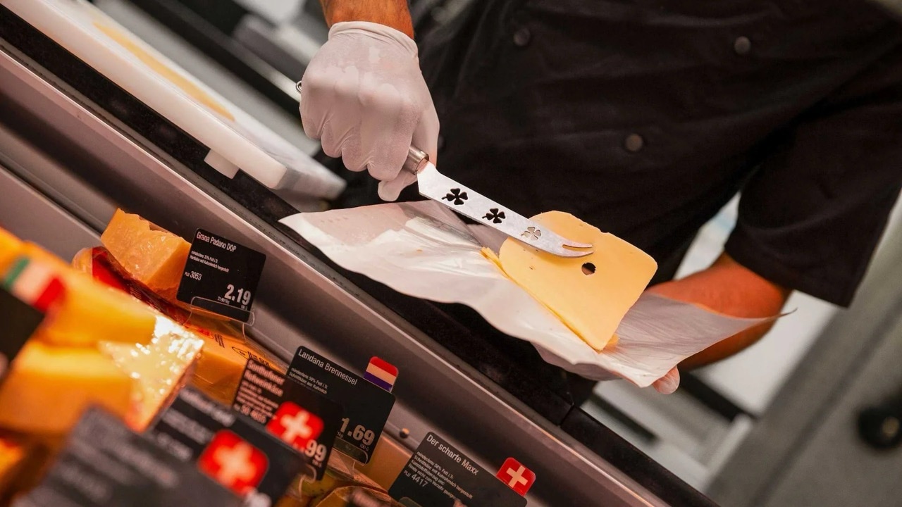 Nahaufnahme der Hände eines Mannes der Käsescheiben mit einem Messer schneidet.