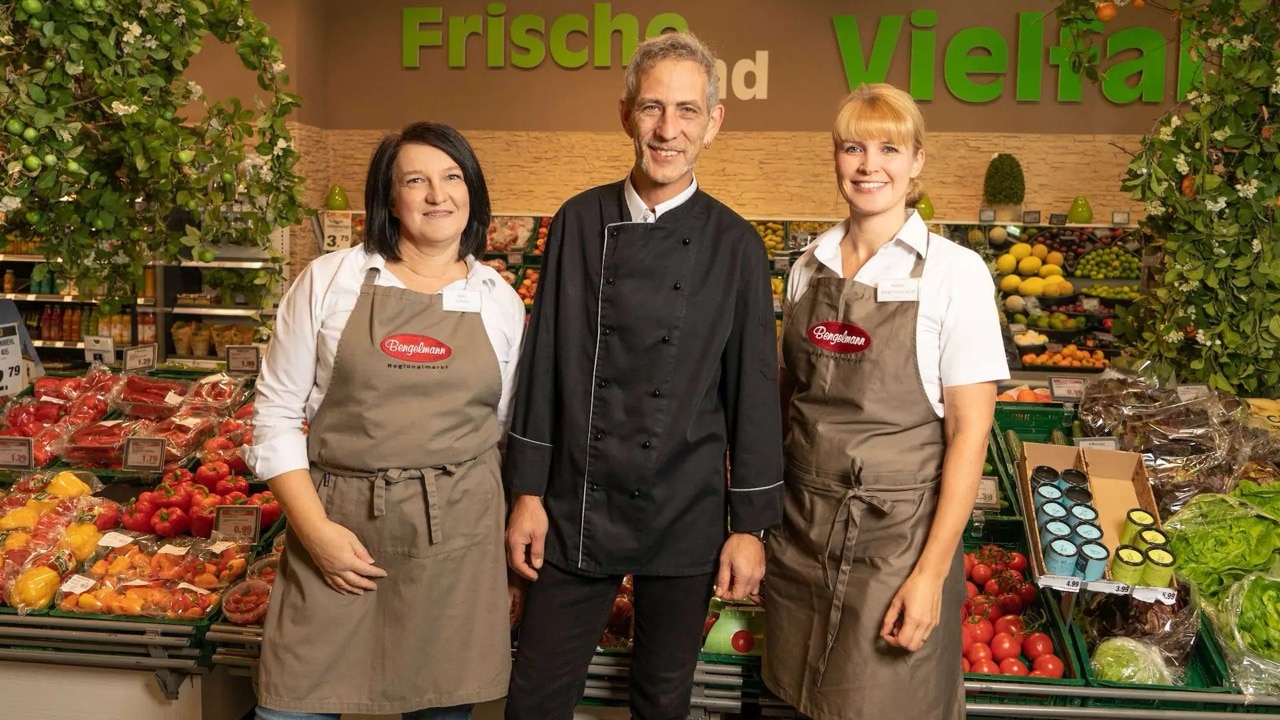 Drei Mitarbeitende eines Edeka-Marktes in der Gemüse-Abteilung.