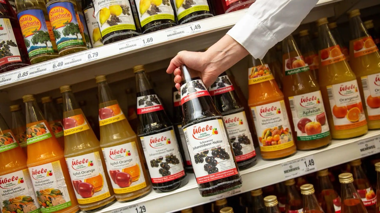 Eine Hand nimmt eine Flasche Johannisbeer-Nektar aus einem Regal.