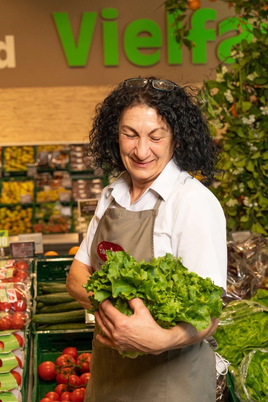 Eine Mitarbeiterin eines Edeka-Marktes hält einen Salatkopf in den Händen.