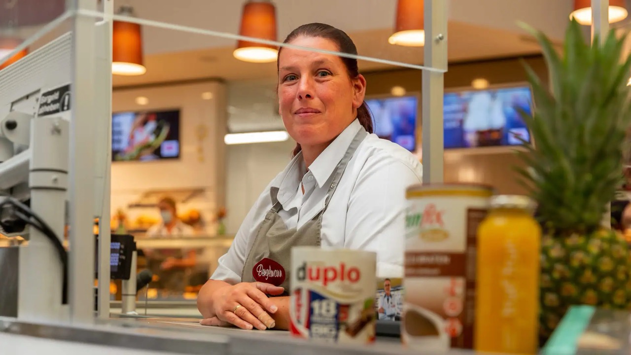 Eine lächelnde Mitarbeiterin sitzt an der Kasse eines EDEKA-Marktes.