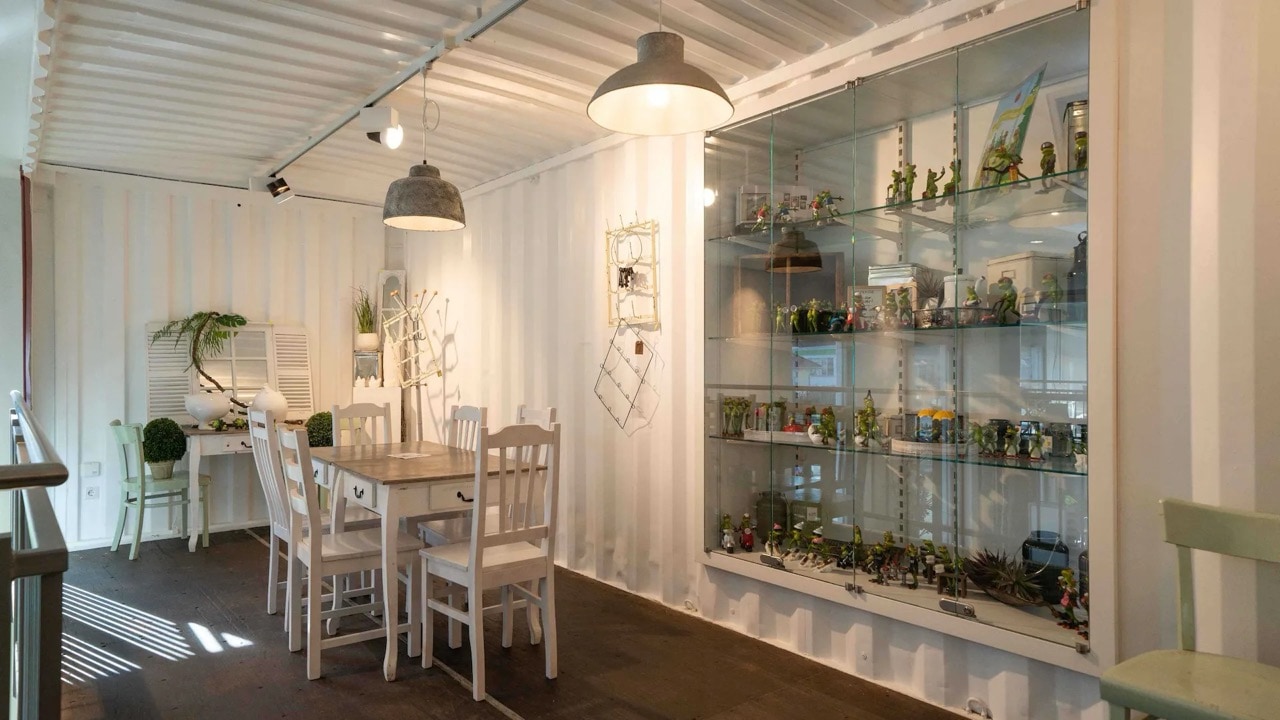 Innenraum eines Cafés in einem umfunktionierten Container. An der Wand ist eines Vitrine mit Froschfiguren aller Art eingelassen.