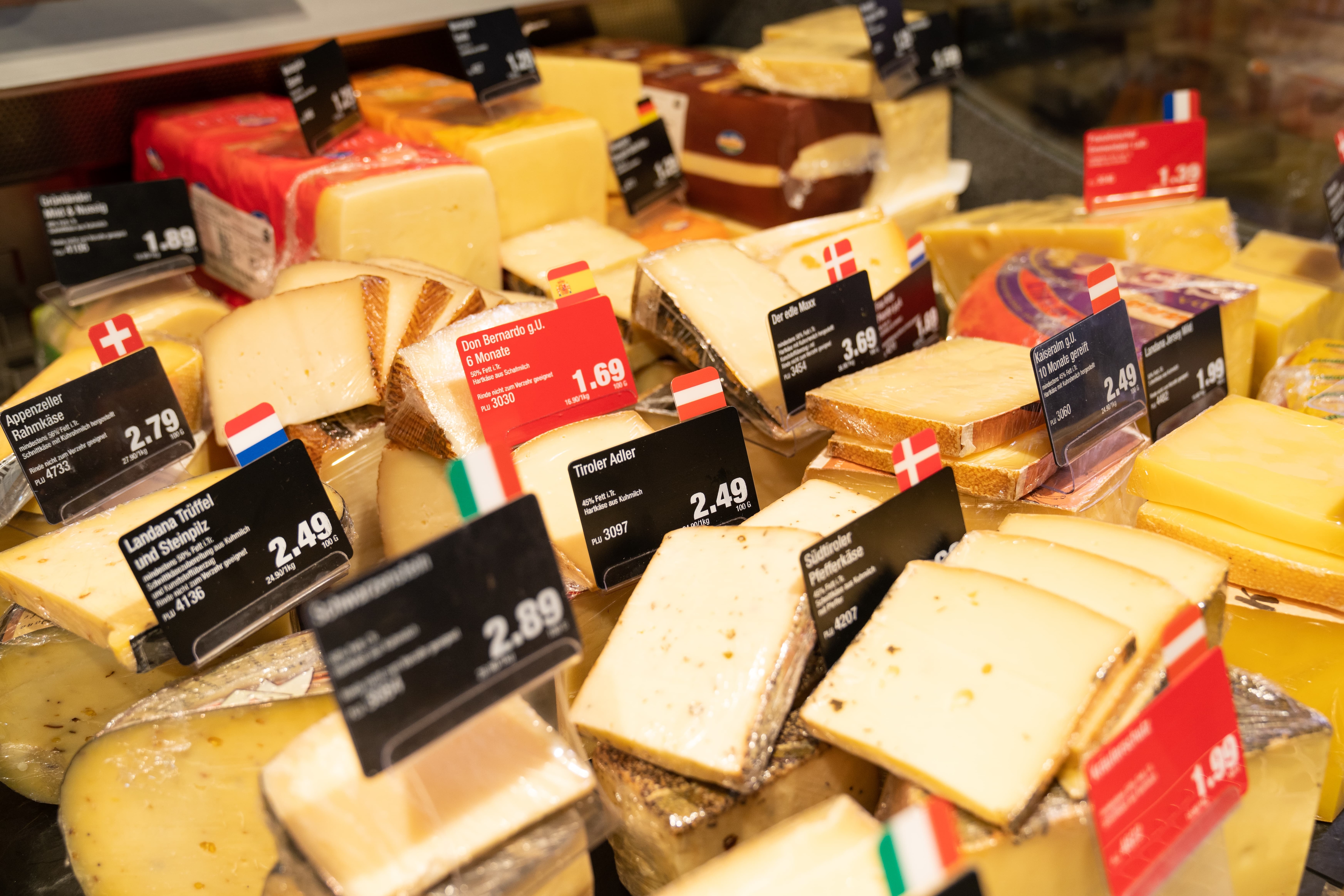 Verschiedene Käsesorten mit Preisschildern in einer Auslage.
