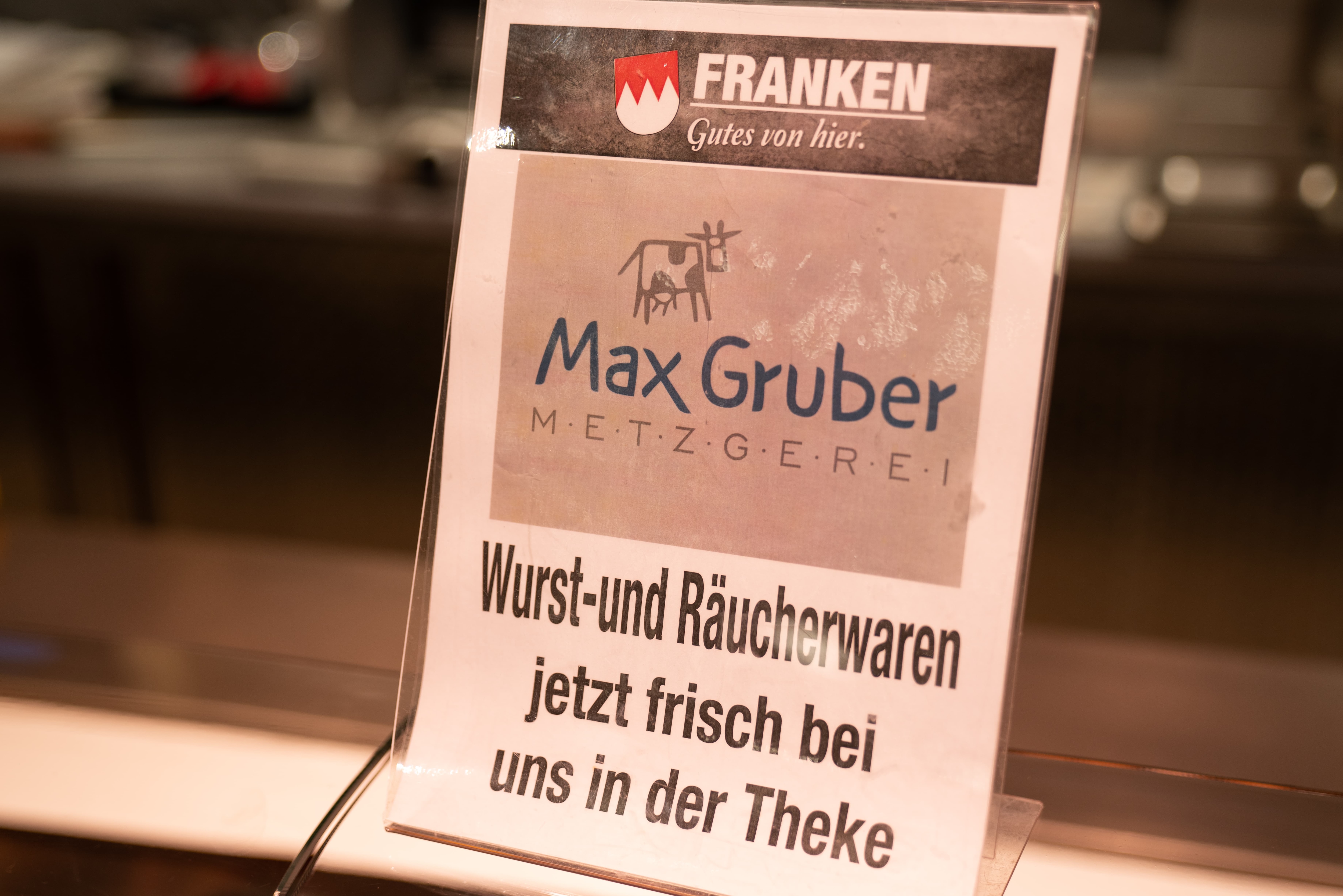 Aufstellschild mit Text: Max Gruber Metzgerei. Wurst- und Räucherwaren jetzt frisch bei uns in der Theke.