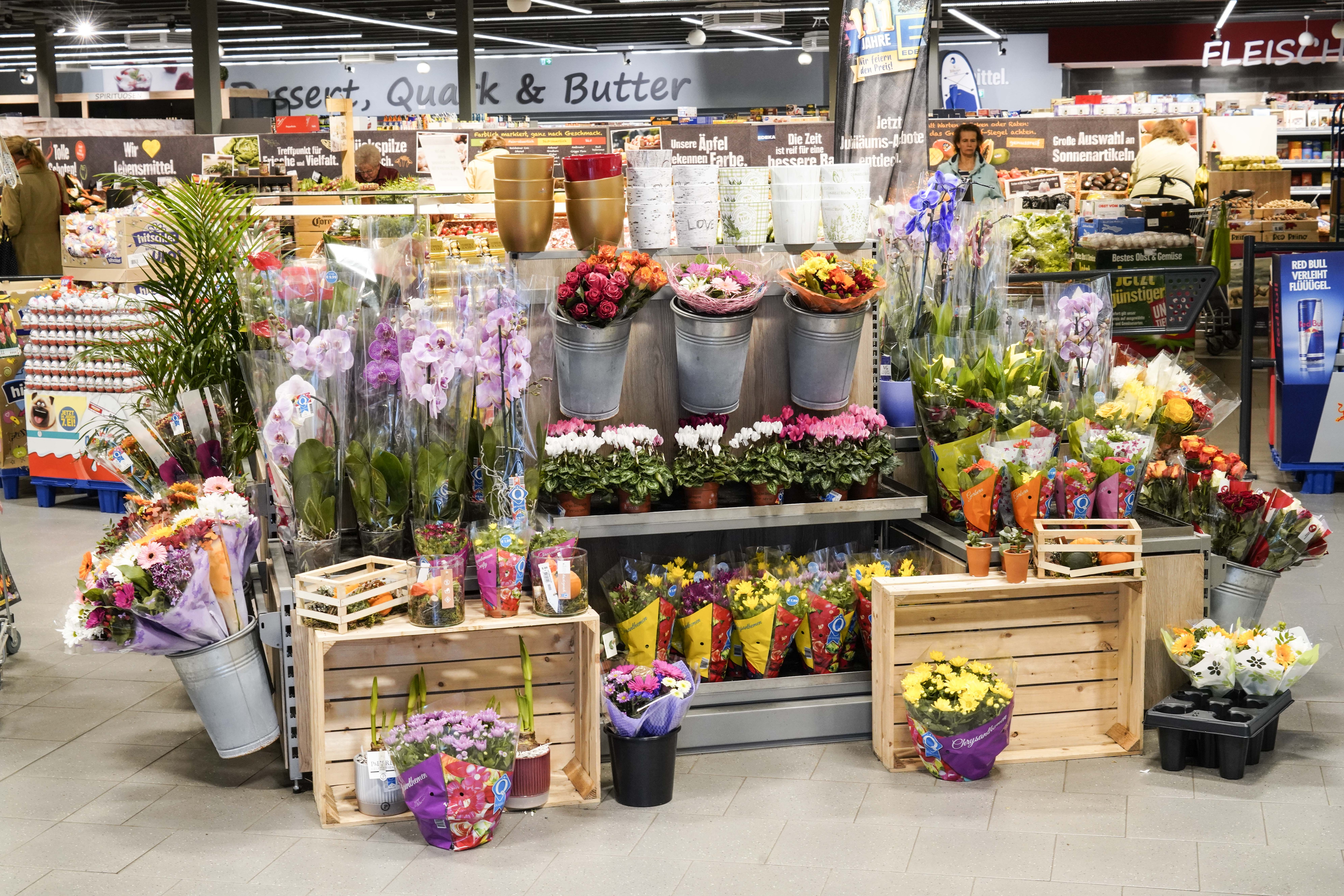 Eine Auslage mit Blumen in Kübeln und Sträußen im Eingangsbereich eines EDEKA-Markts, in vielen Farben und Sorten.