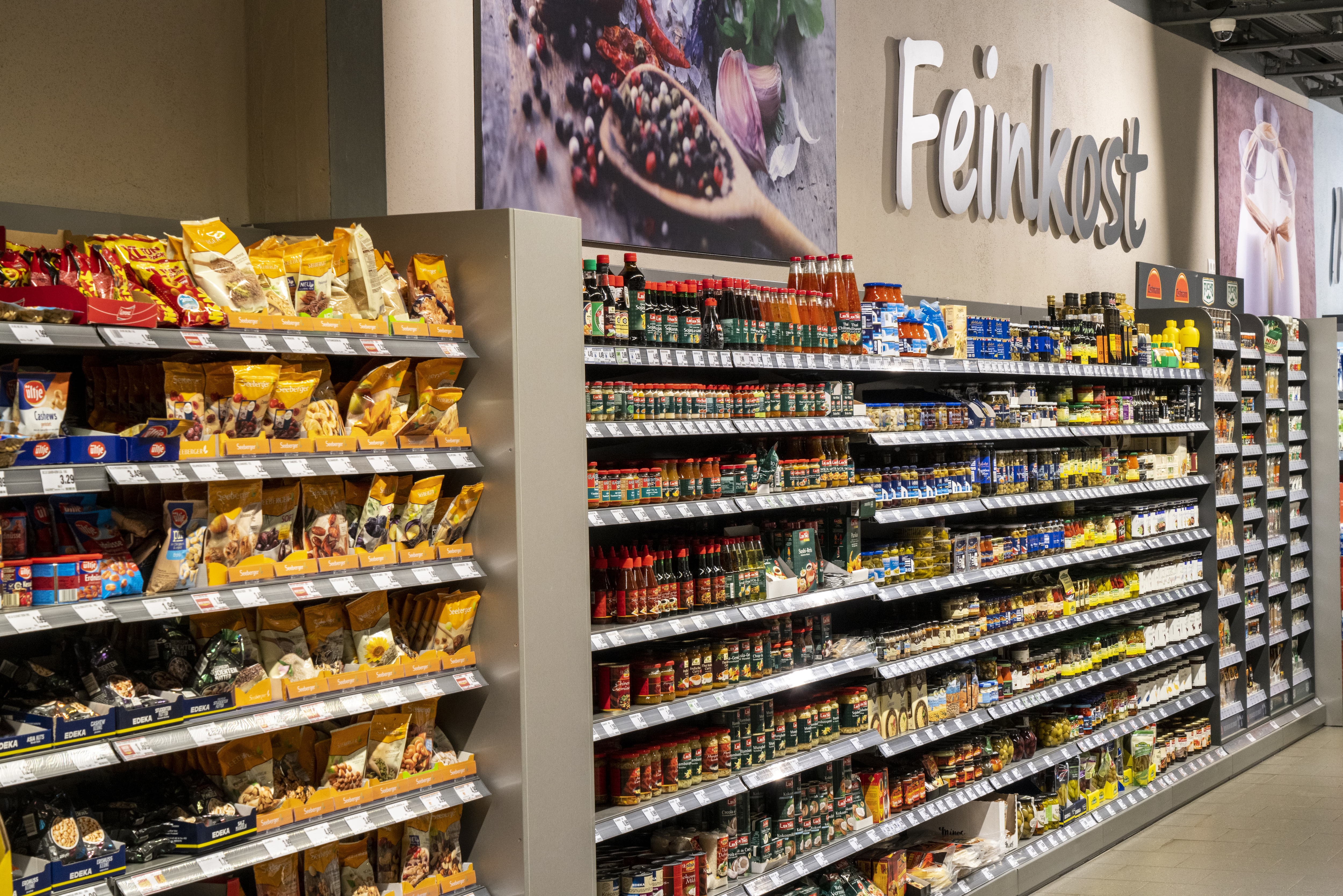 Feinkostabteilung des EDEKA-Markts mit Nussmischungen auf der linken Seite und asiatischen Soßen und Würzpasten im mittleren Bereich.