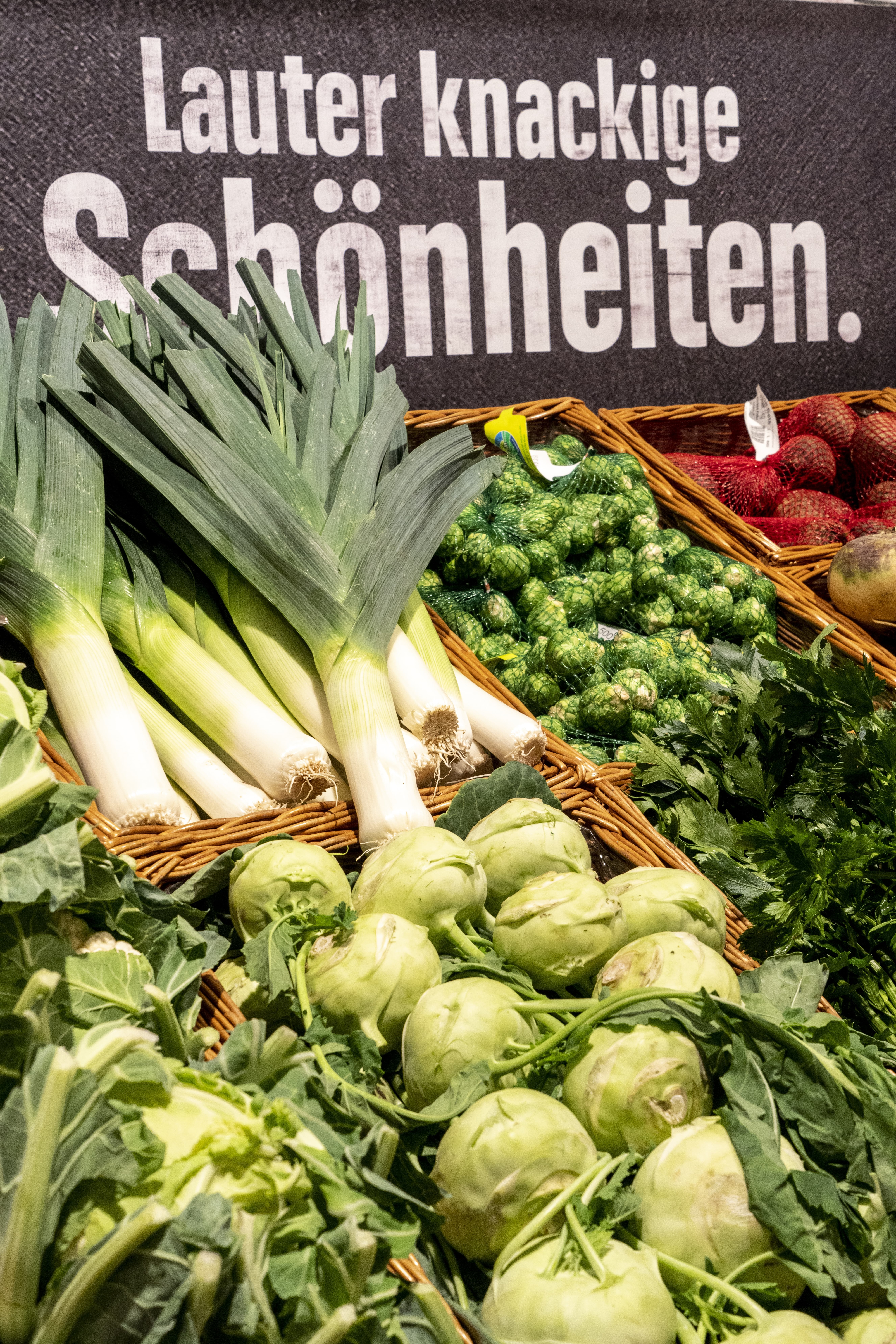Gemüseabteilung eines EDEKA-Markts mit grünen Gemüsesorten im Fokus und der Aufschrift „Lauter knackige Schönheiten“ im Hintergrund.
