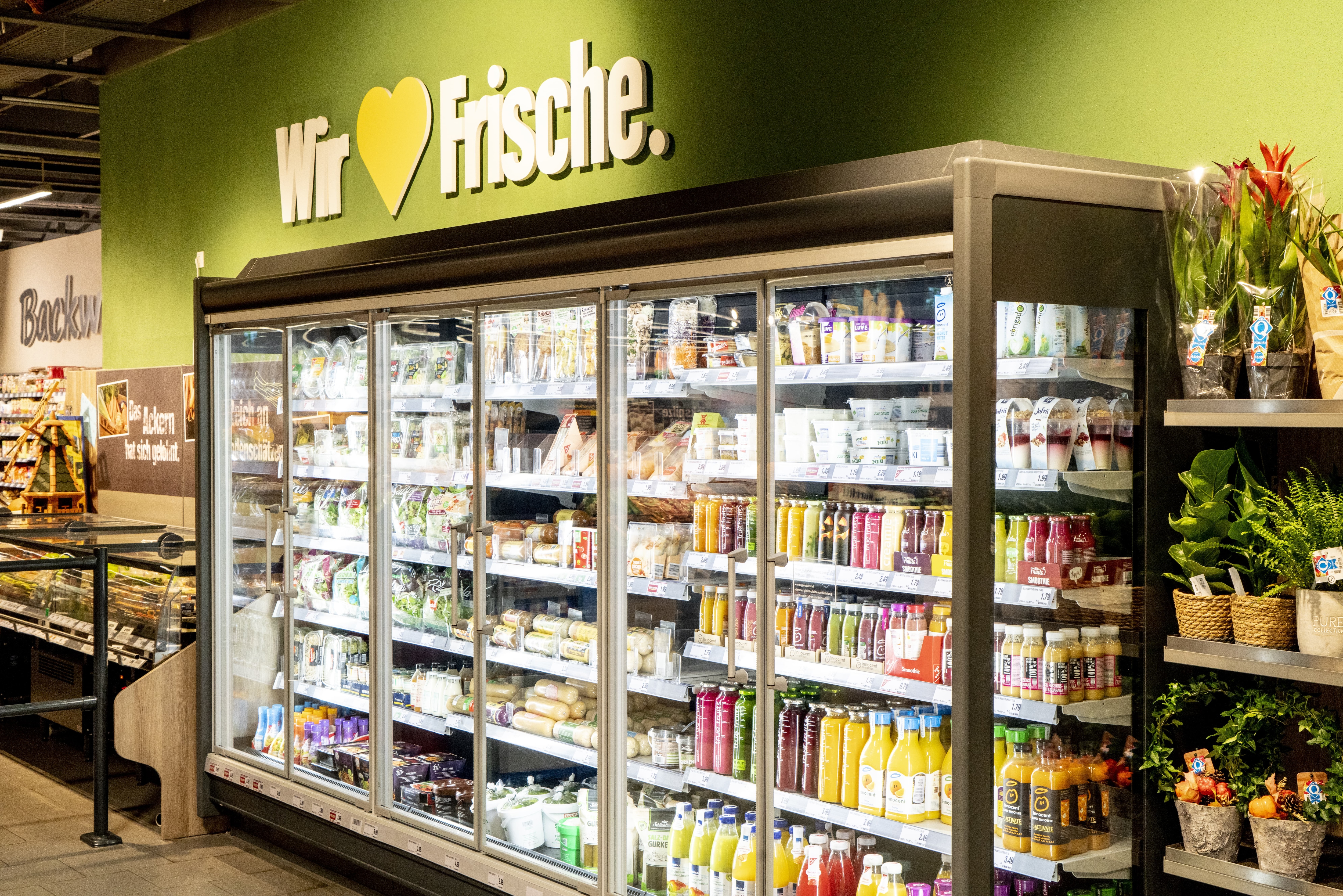 Ein Kühlregal mit Smoothies, darüber an der Wand der Schriftzug: „Wir lieben Frische“.