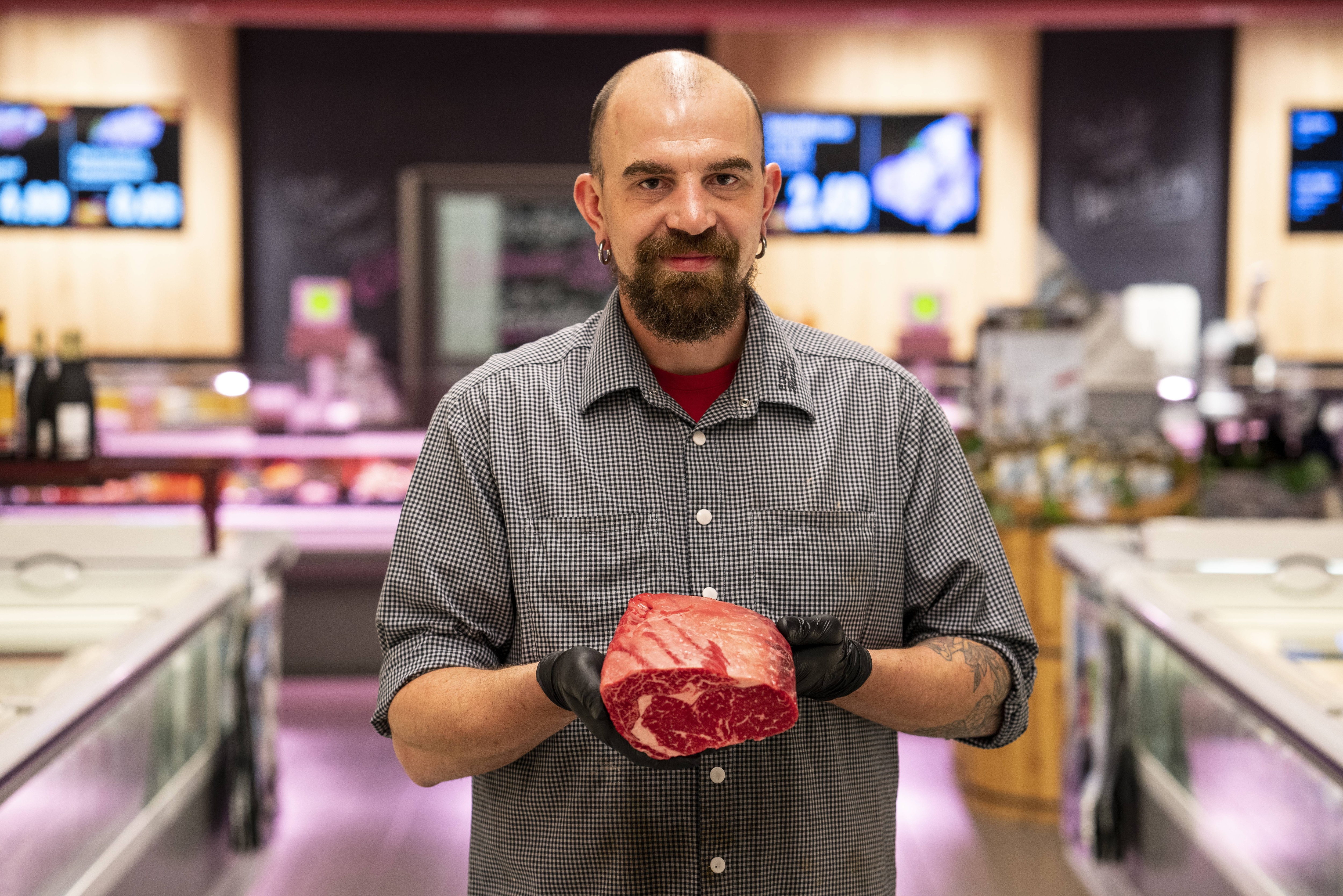 Ein lächelnder Mitarbeiter der Fleischtheke hält ein Stück Fleisch in den Händen.