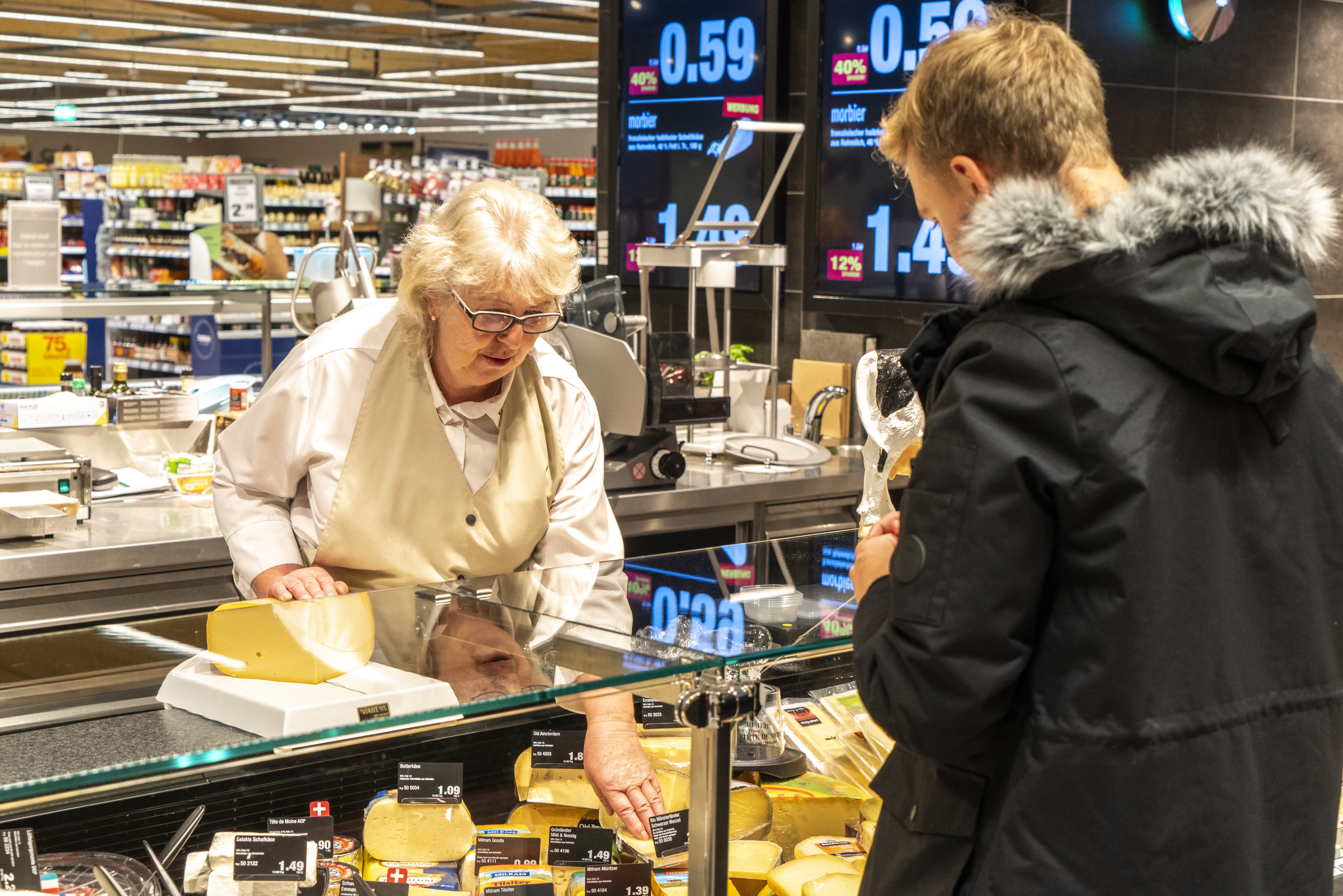 Eine Edeka-Mitarbeiterin berät einen Kunden an der Käsetheke.