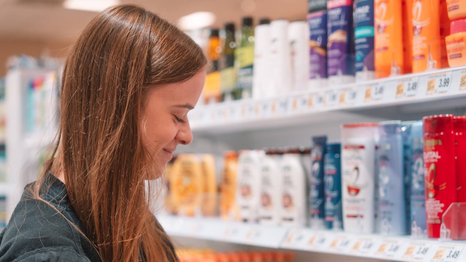 Eine Mitarbeiterin im Profil am Drogerieregal, die nach unten blickt.