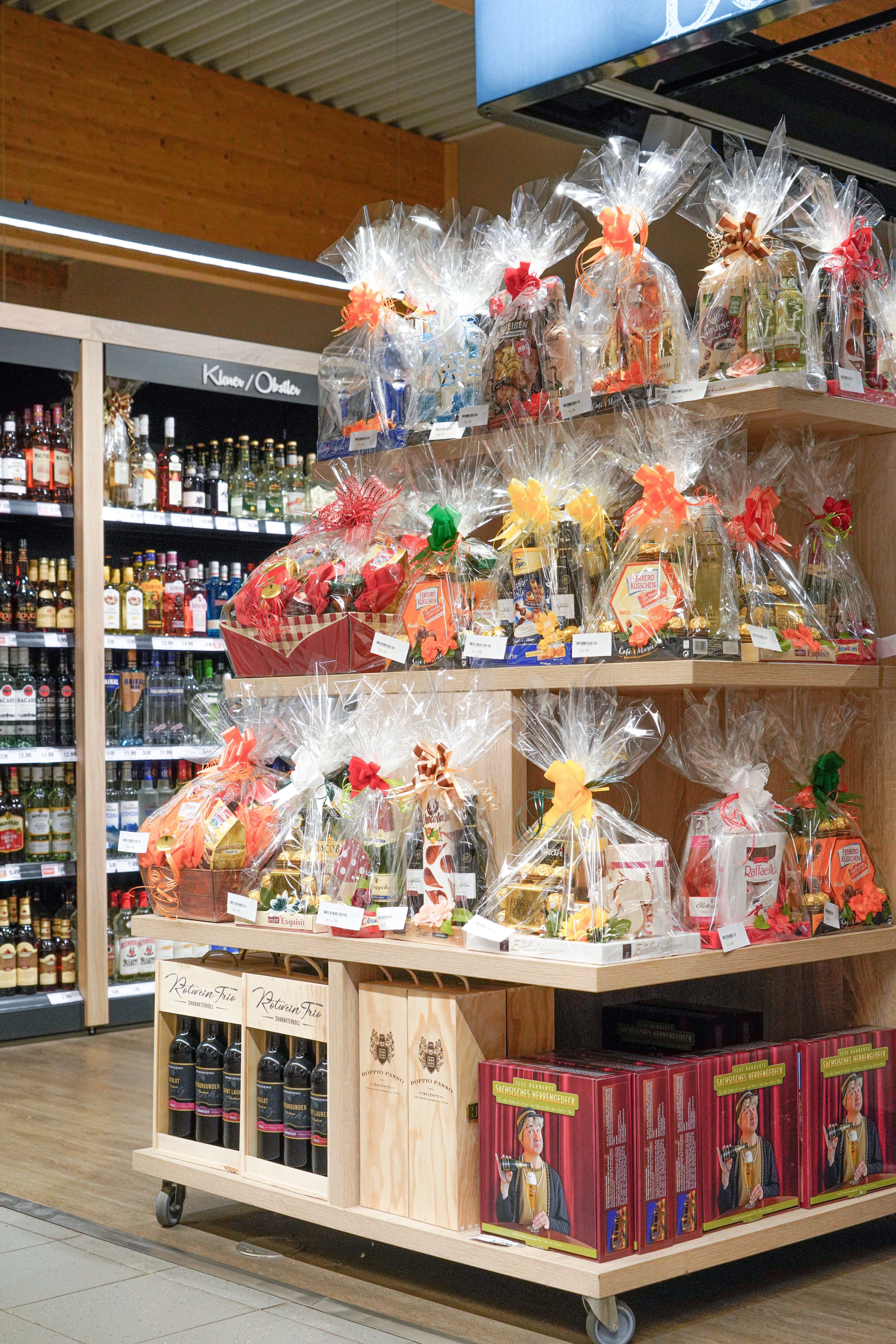 In Plastikfolie verpackte und mit Schleifen verzierte Präsentkörbe auf einem Regal in einem EDEKA-Markt.