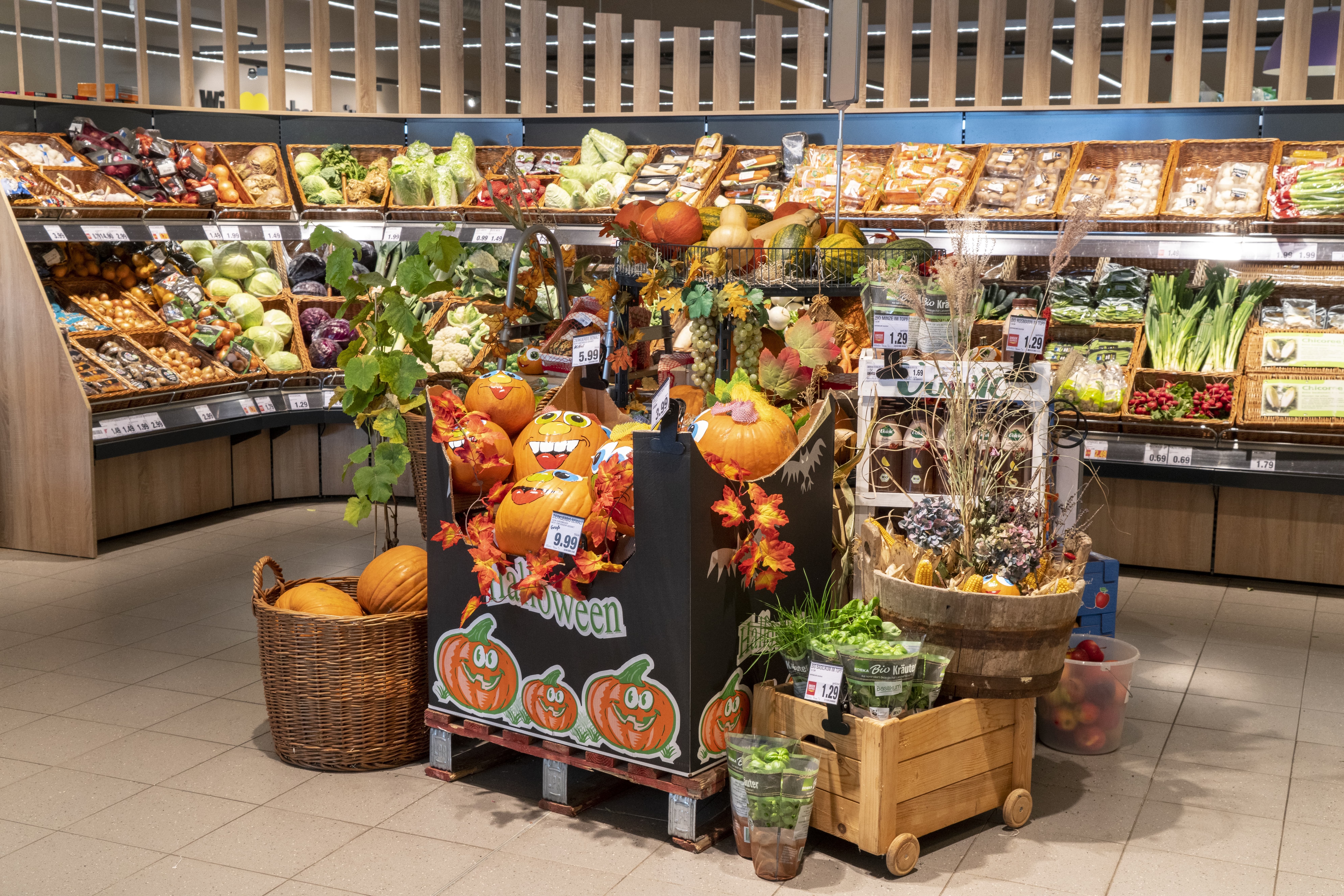 Die Obst- und Gemüseabteilung eines EDEKA-Markts mit einer herbstlich dekorierten Produktinsel im Vordergrund, darauf Kürbisse, Küchenkräuter und Äpfel.