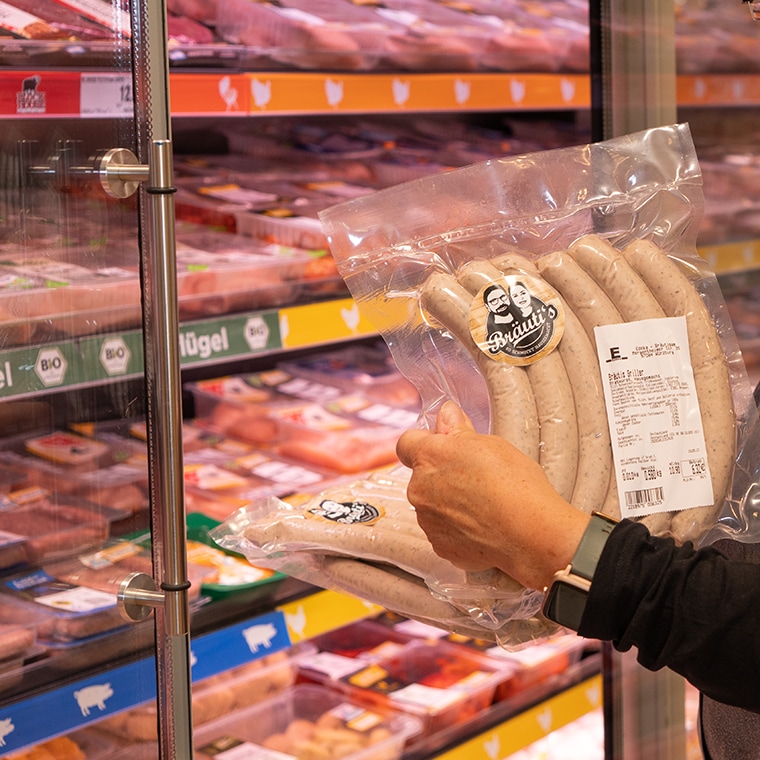 Eine Hand hält eine Packung Bratwurst in die Kamera.