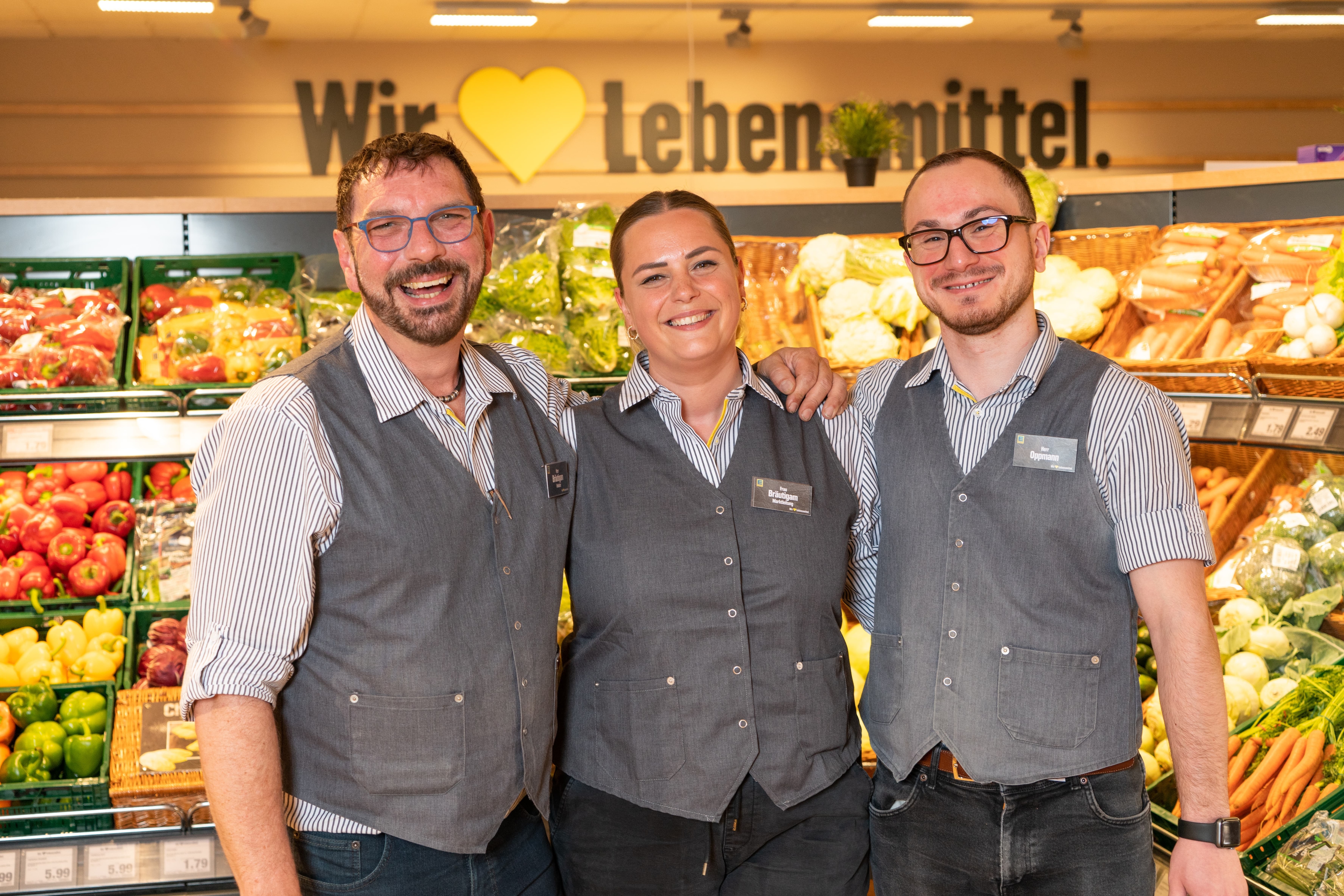 Der Inhaber, die Marktleiterin sowie der stellvertretende Marktleiter eines Edeka-Marktes lächeln in die Kamera.