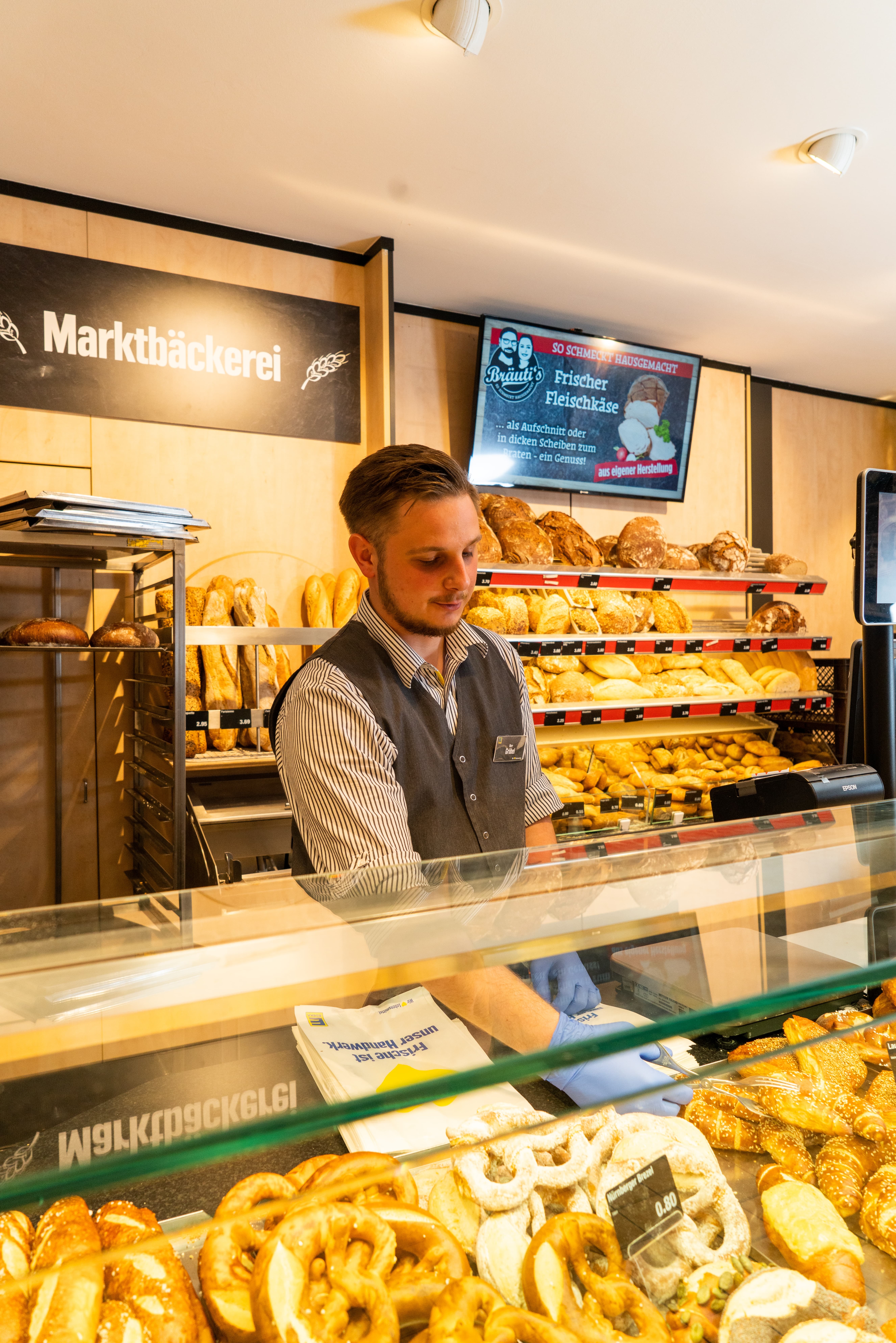Ein Mitarbeiter einer Baeckerei packt Brötchen in eine Papiertüte.
