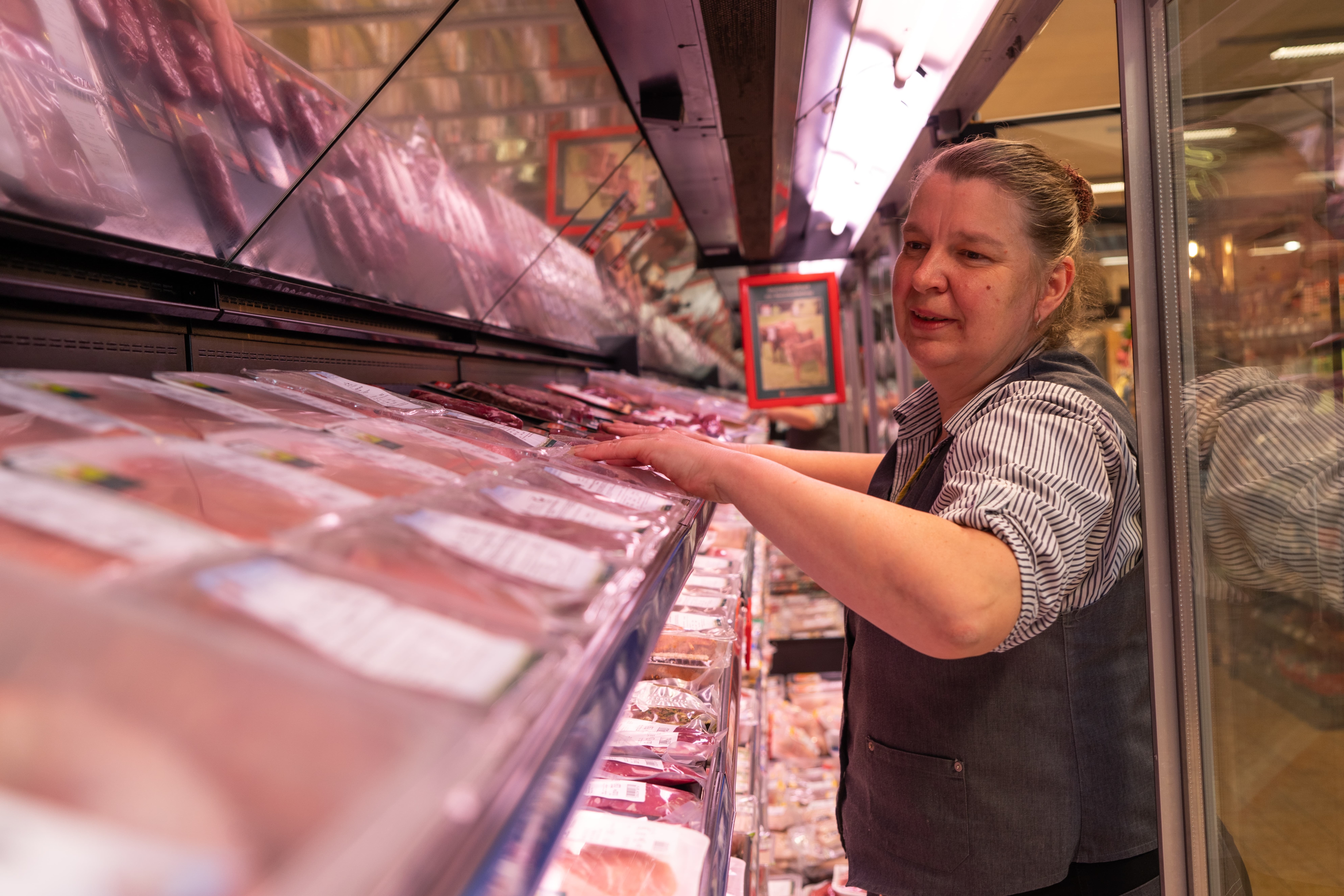 Eine Mitarbeiterin sortiert Fleischprodukte in einem Kühlregal.