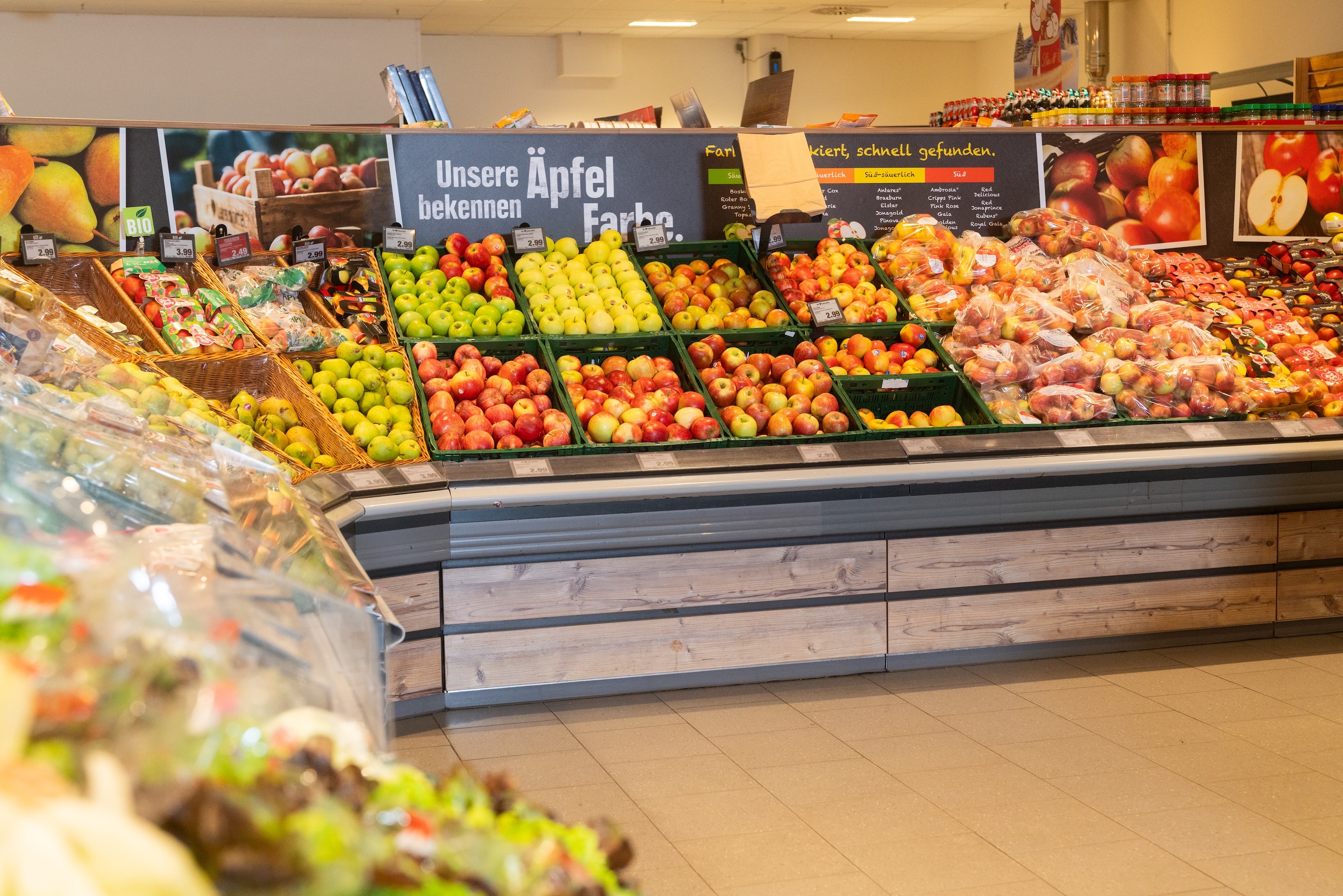 Apfelauslage im Supermarkt. An der Wand steht „unsere Äpfel bekennen Farbe.“