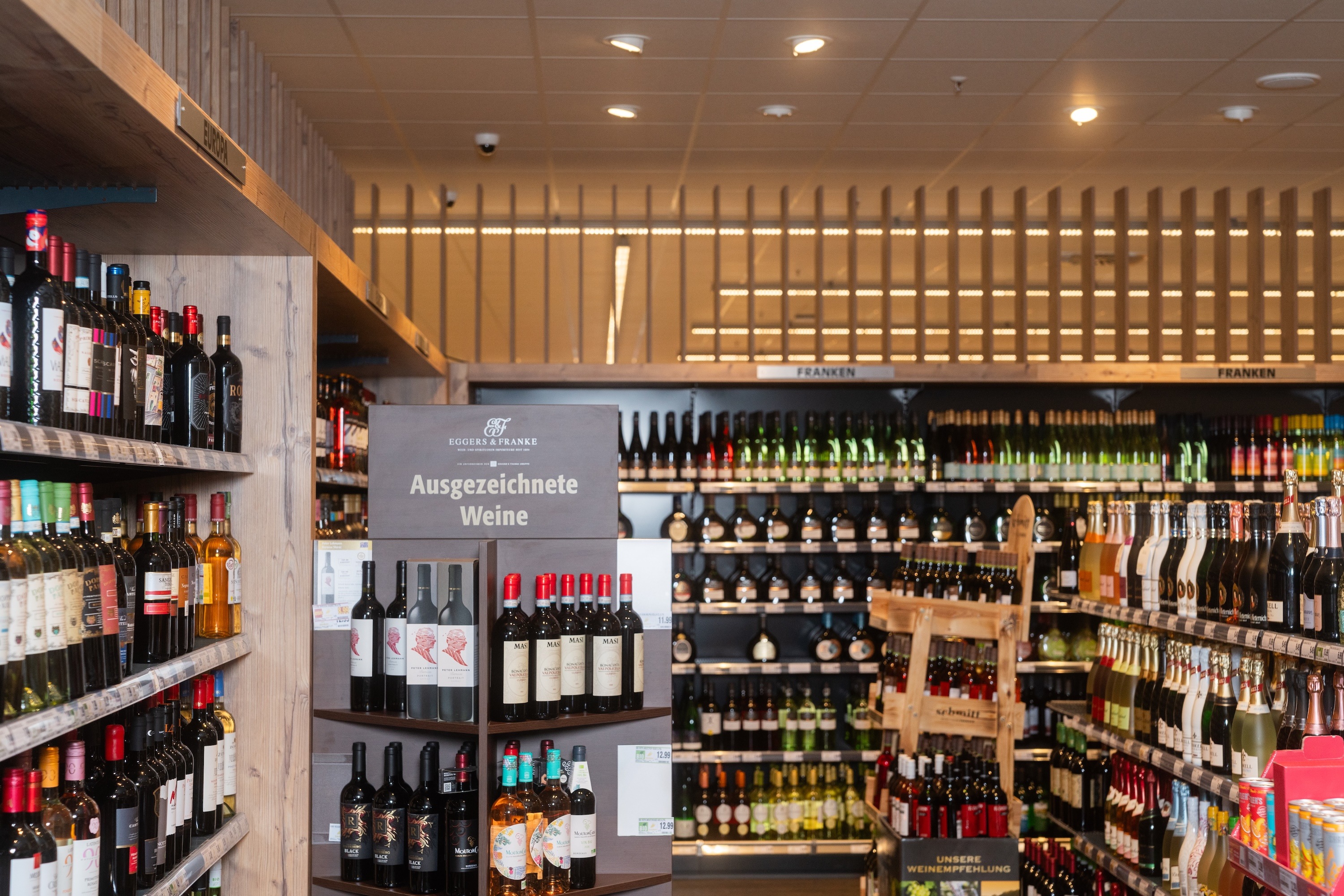 Weinregal im Supermarkt. Auf einem Aufsteller steht „Ausgezeichnete Weine“.