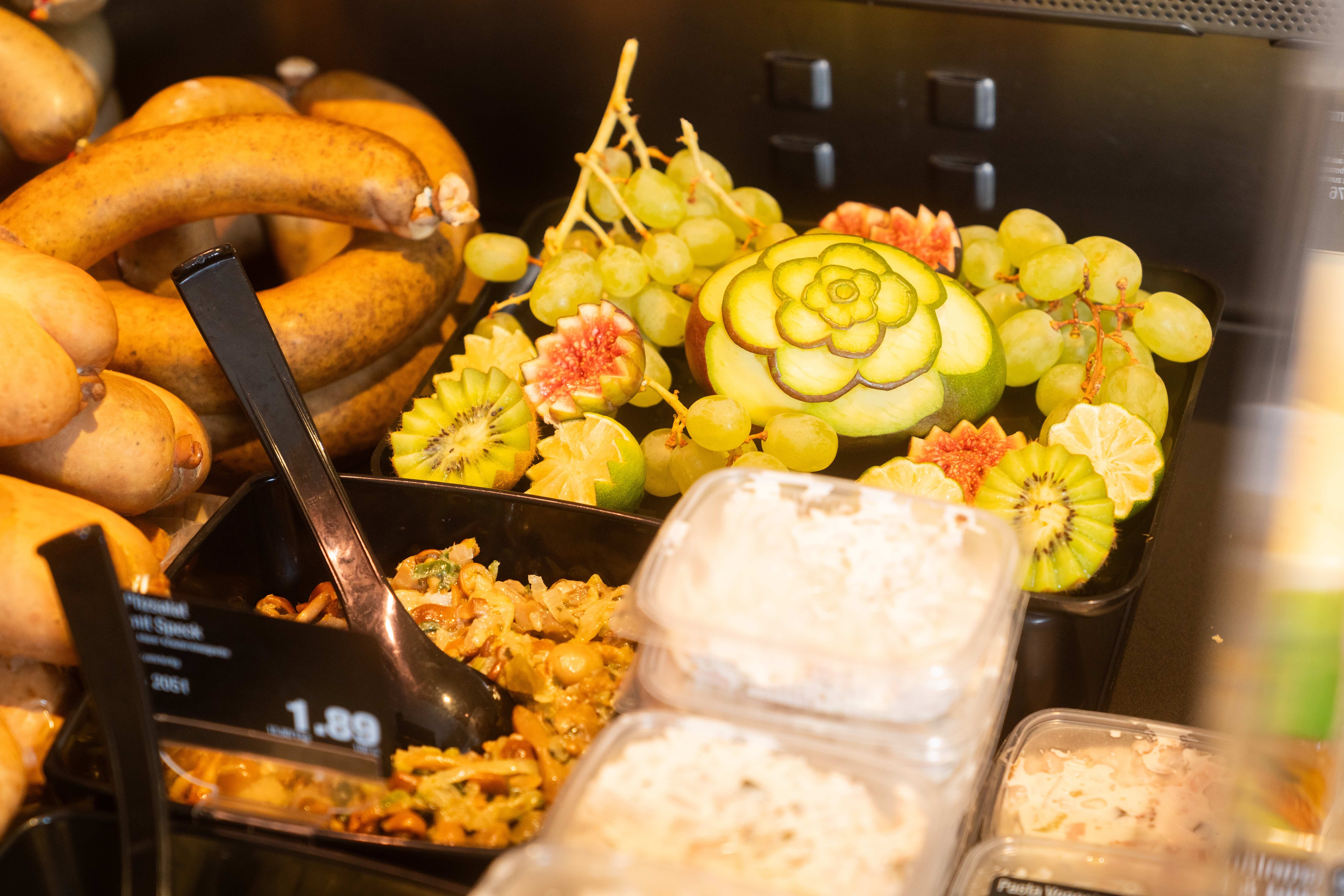 Teil der Auslage an der Frischetheke mit selbstgemachten Salaten und geschinitzem Obst und Würsten.