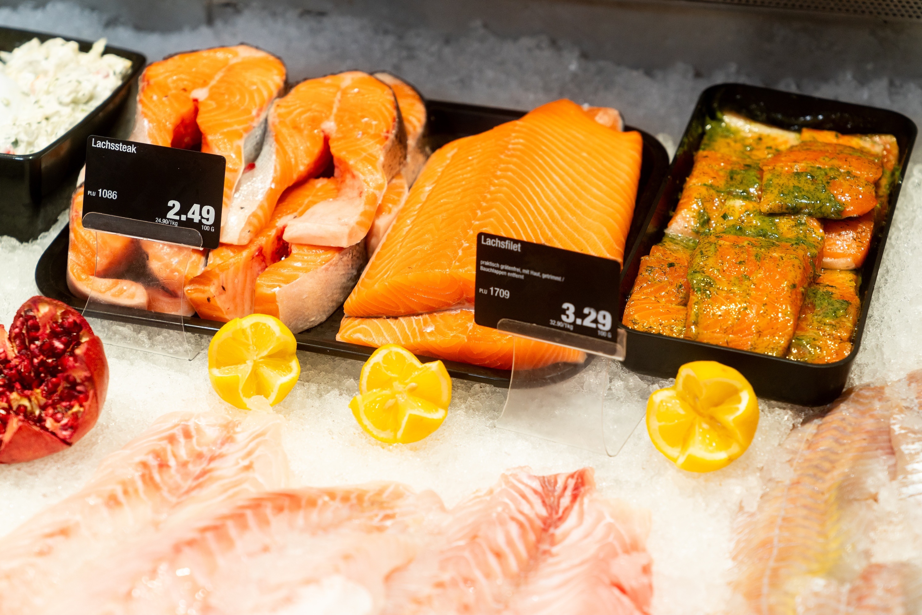 Lachs in verschiedenen Varianten in Auslage mit Eis unter den Behältern.