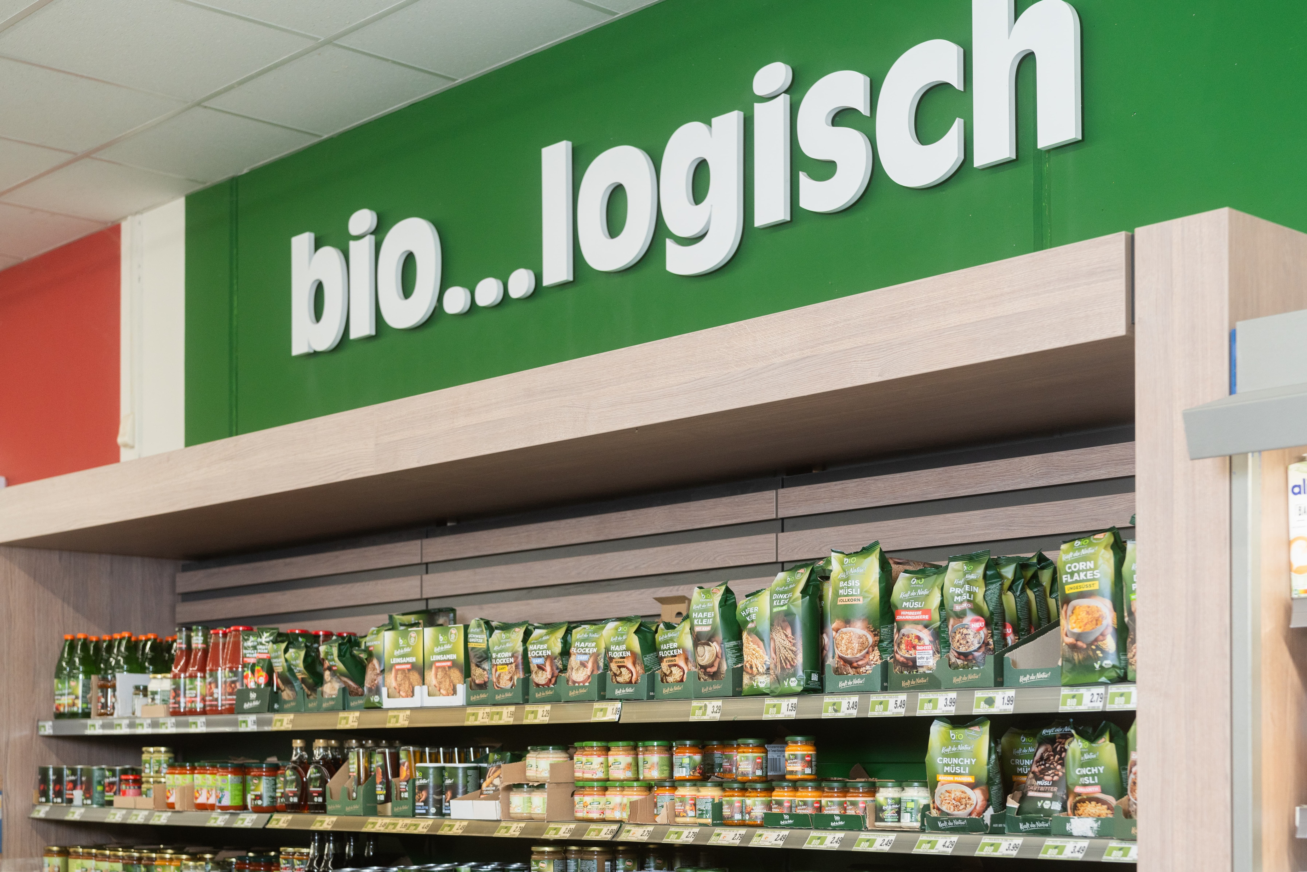 Regal mit vielen grün verpackten Lebensmitteln. Über dem Regal steht bio...logisch mit weißen Buchstaben auf grünem Grund.