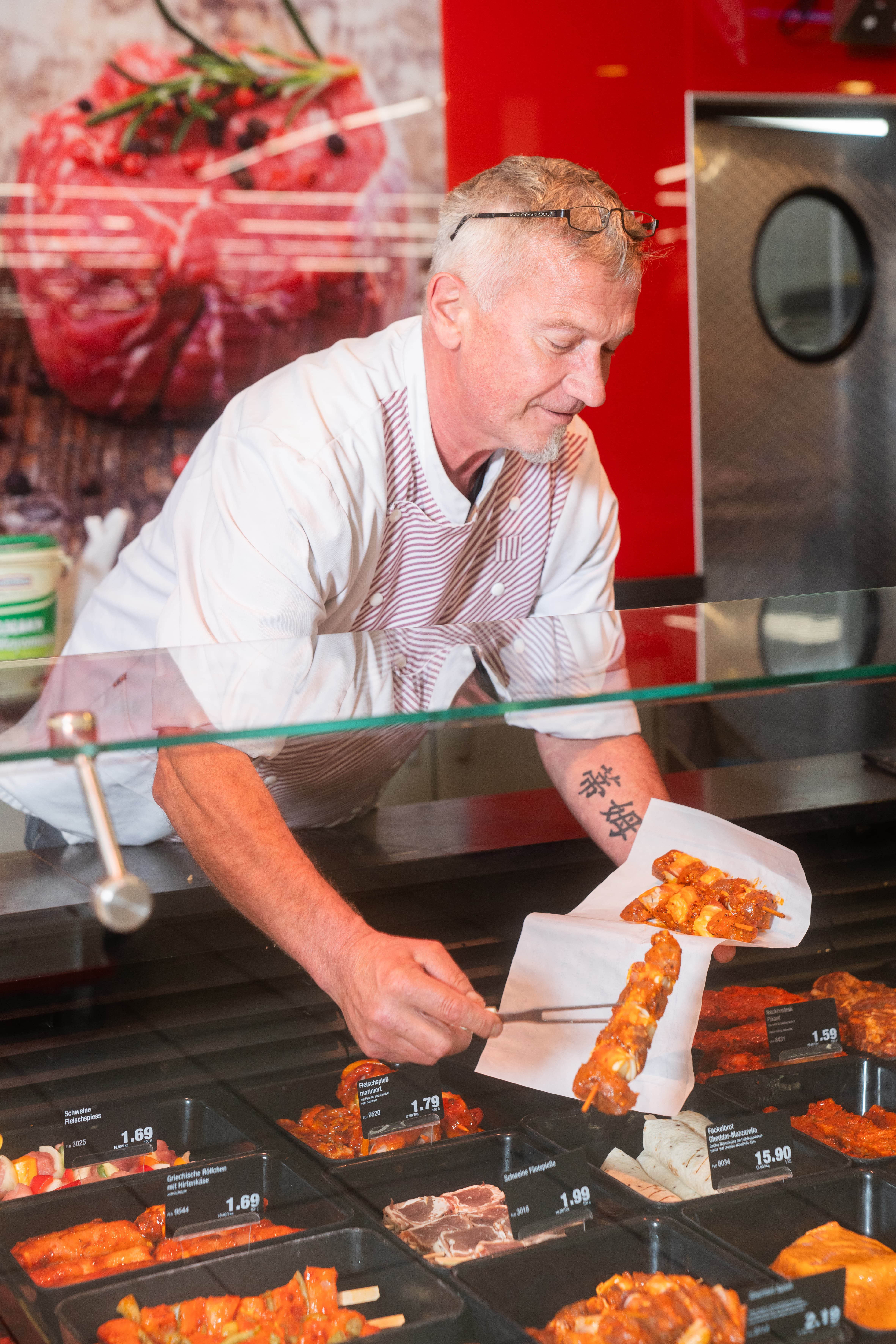 Ein Mann in Arbeitskleidung packt Fleischspieße in ein Stück Papier.