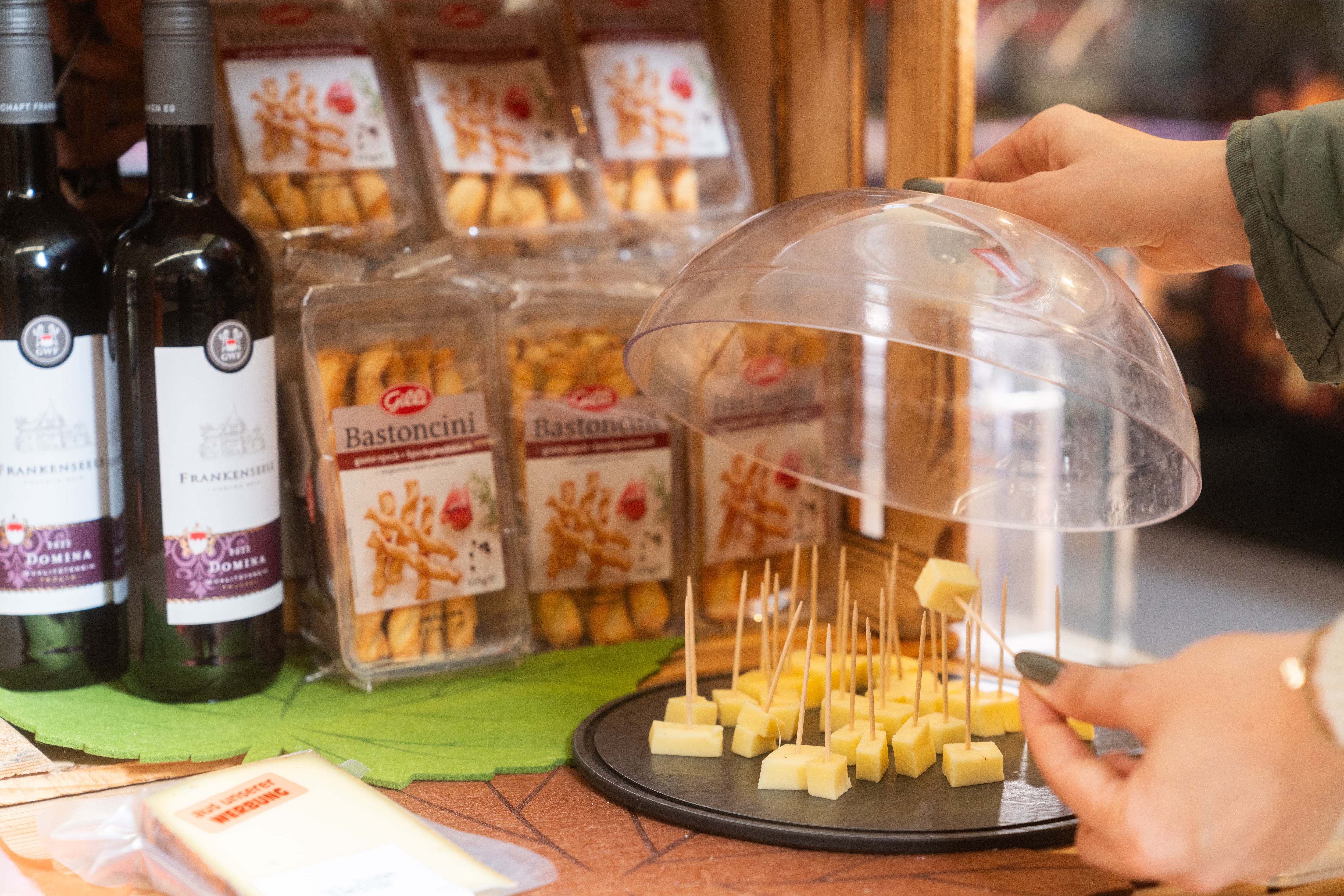 Eine Käseglocke mit angehobenem Deckel. Auf dem Teller liegen Käsewürfel, die mit Zahnstochern aufgespießt sind.