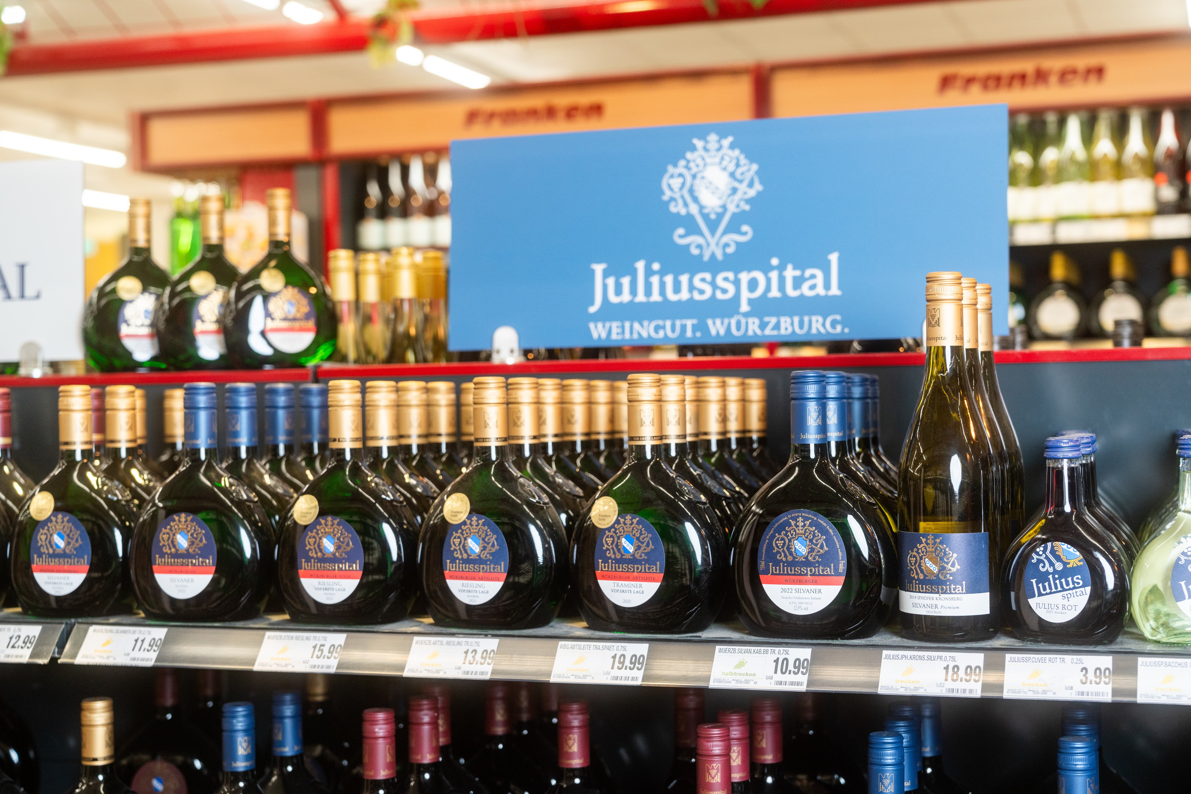 Über einem Weinregal mit rundlichen Flaschen steht Juliusspital Weingut Würzburg geschrieben.