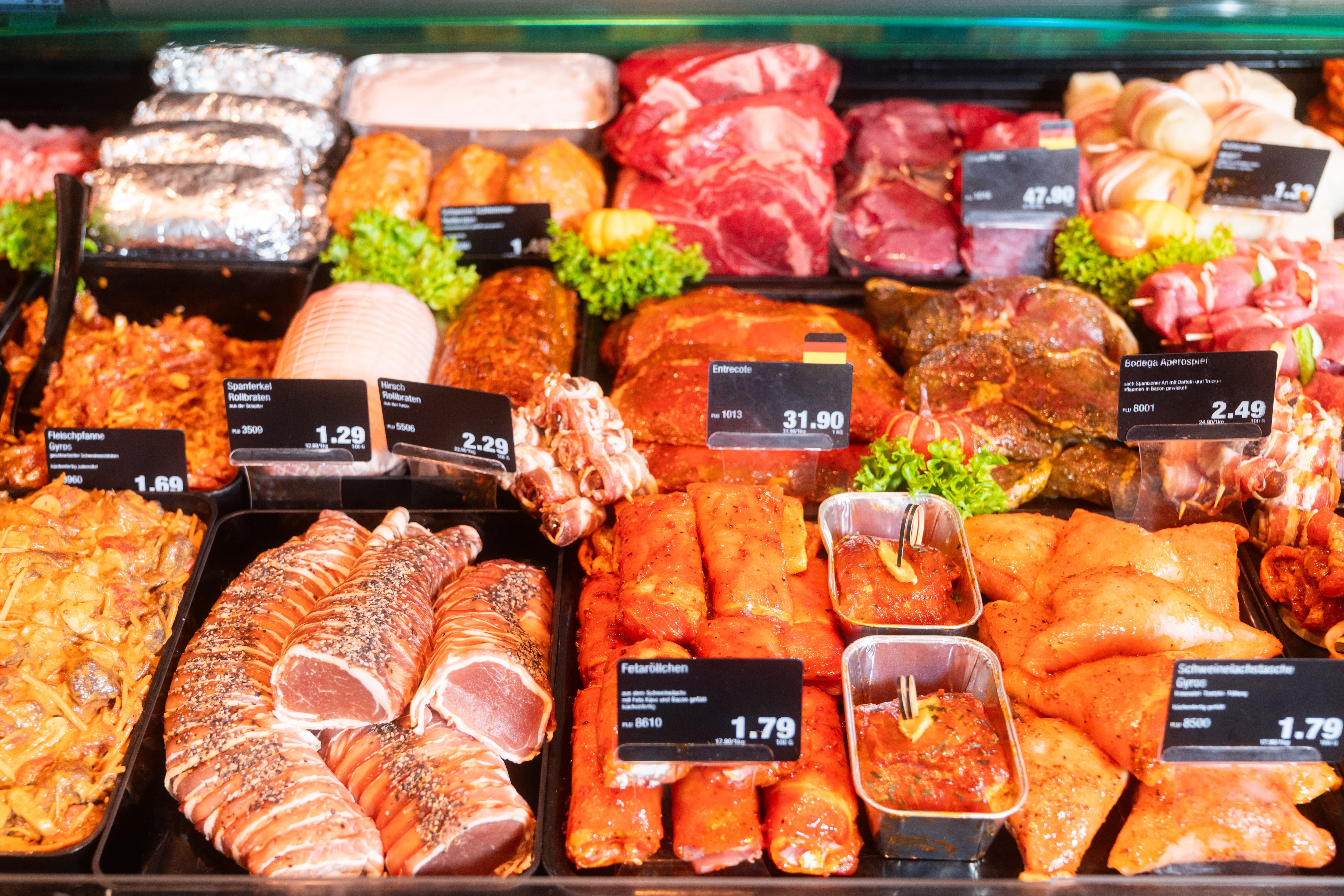 Verschiedene marinierte Fleischsorten mit Preisschildern in einer Auslage.