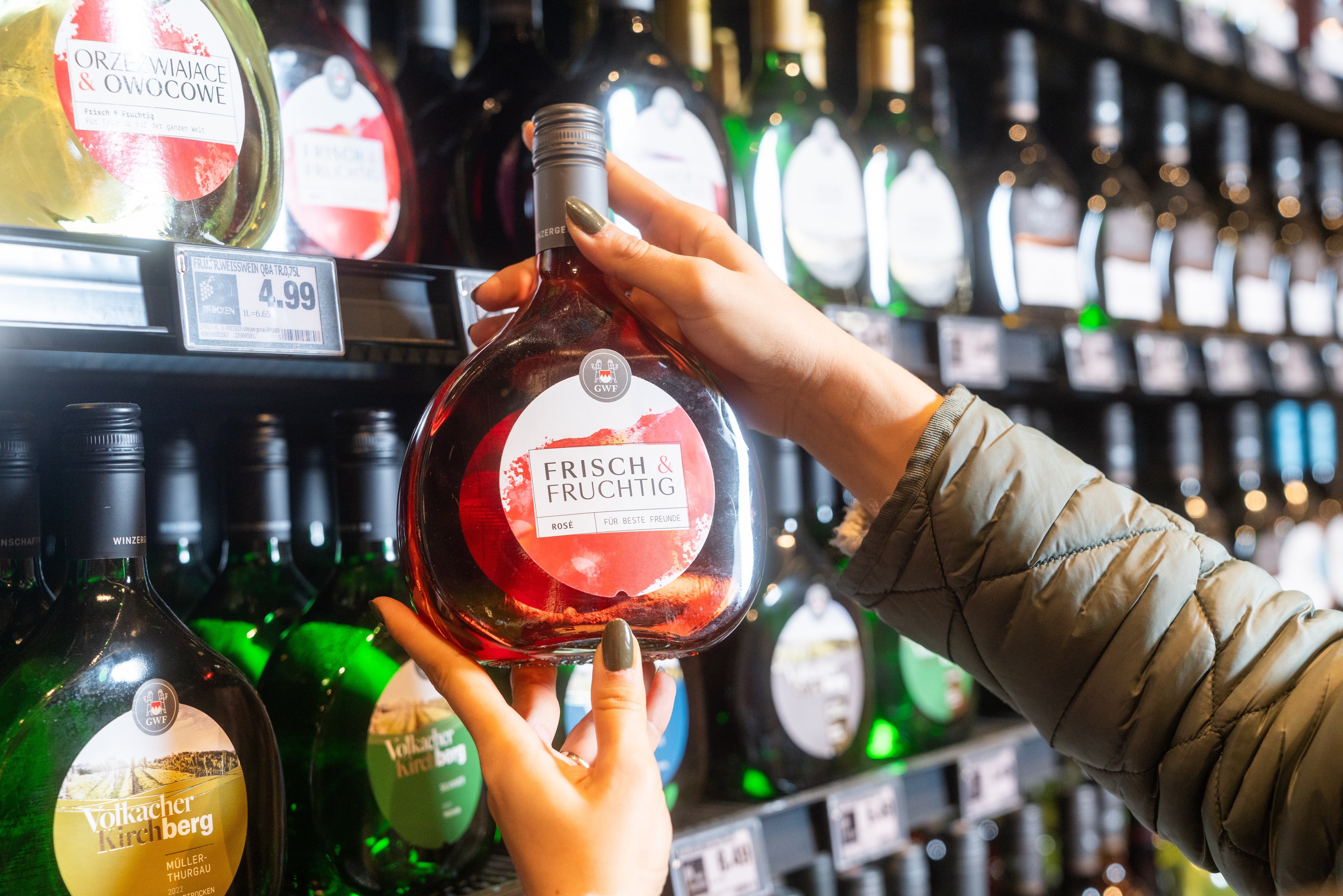 Zwei Hände halten eine rundliche Flasche Roséwein vor einem Regal.