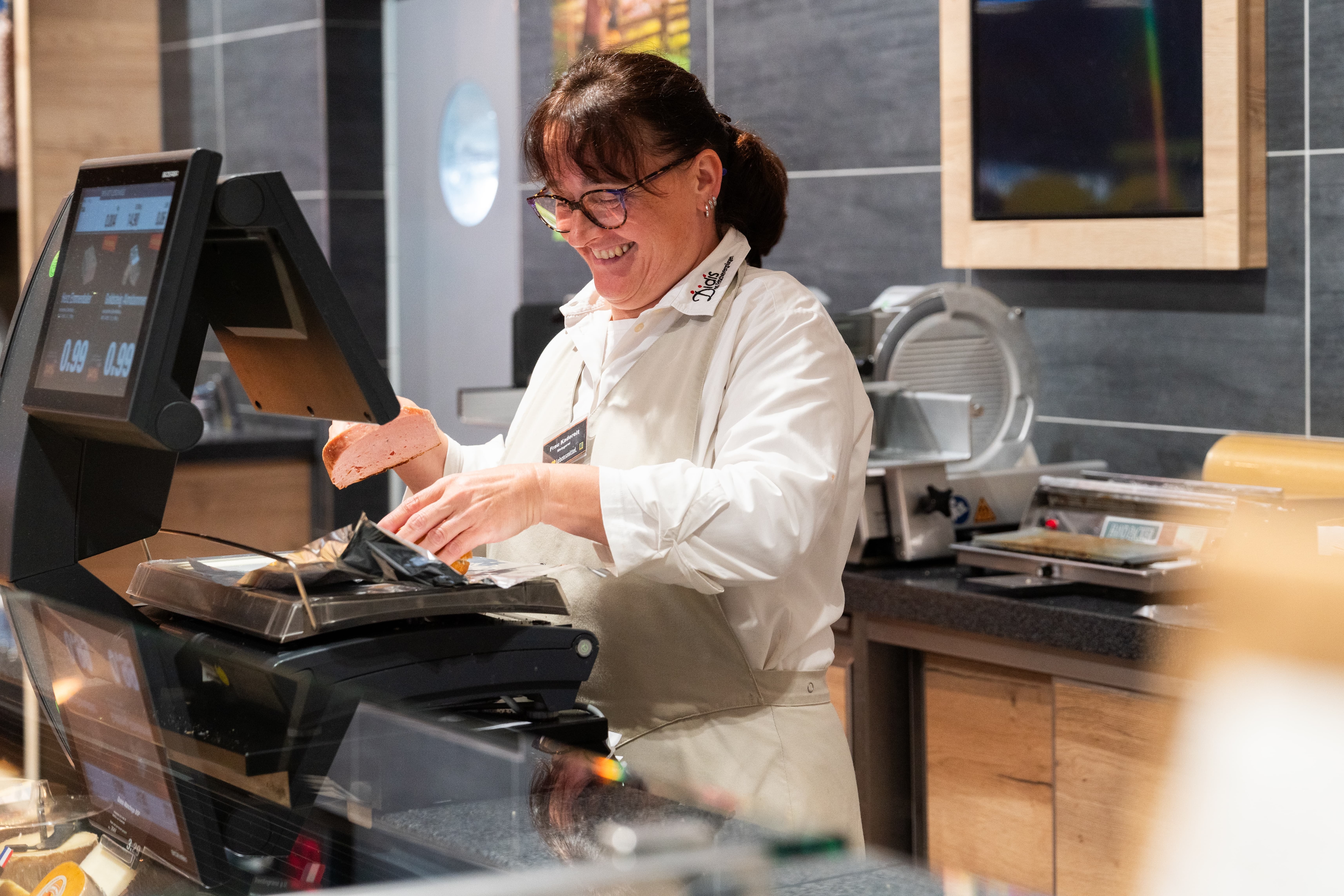 Eine Edeka Mitarbeiterin bei abwiegen von Fleischwaren in der Fleischtheke.