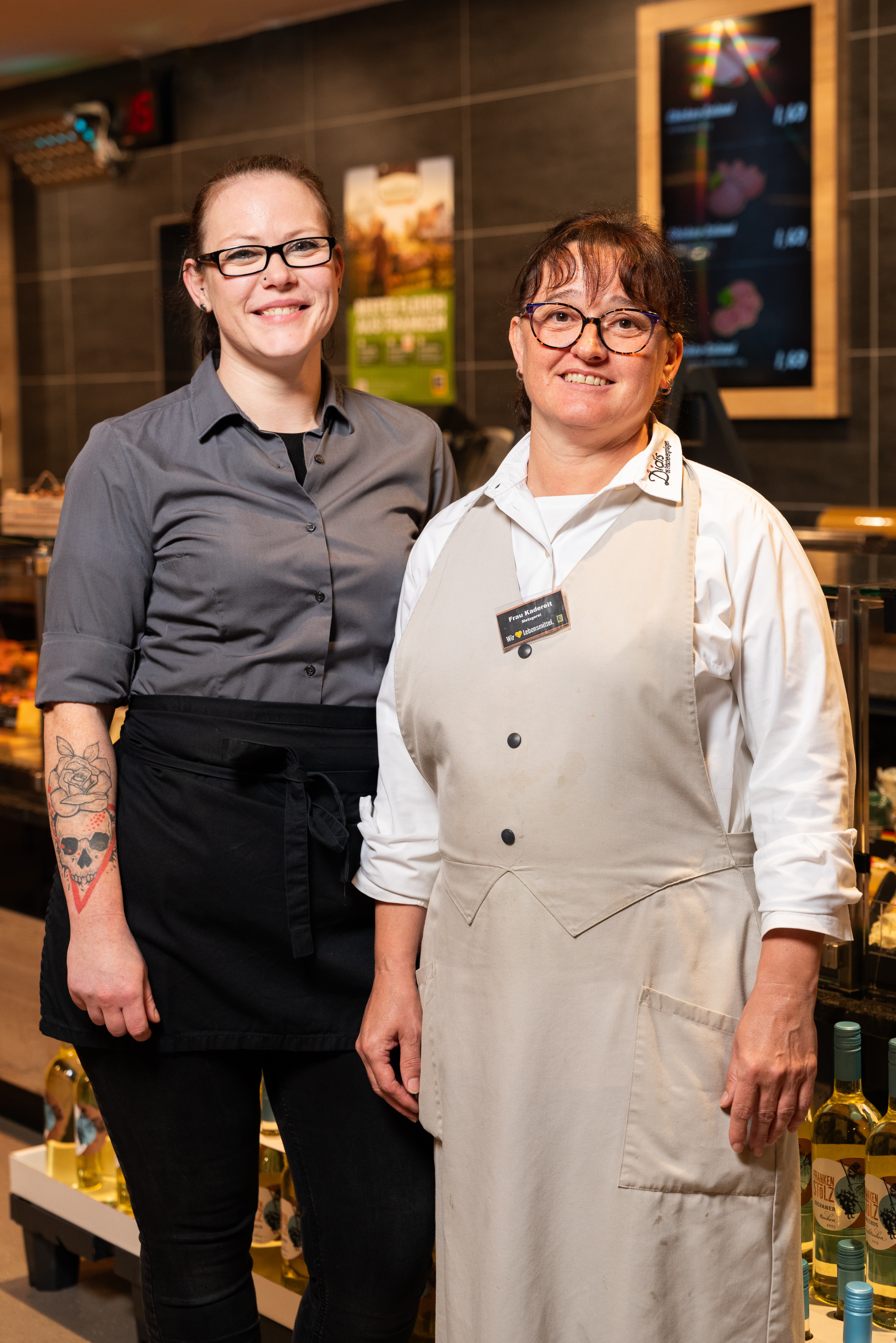 Zwei Edeka Mitarbeiterinnen stehen vor der Frischetheke und lächeln.