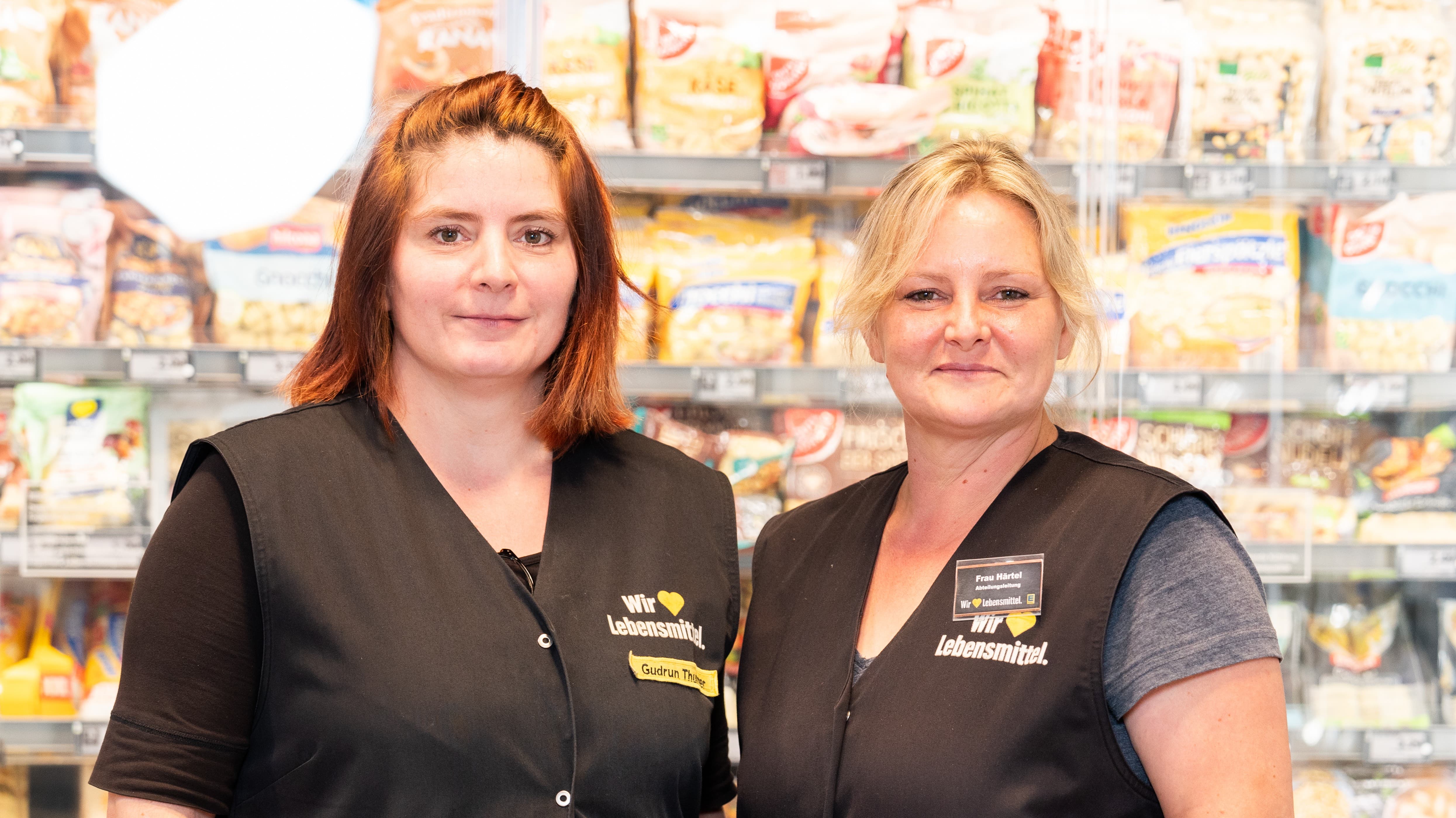 Zwei Edeka Mitarbeiterinnen stehen nebeneinander in der Kühlabteilung und lächeln.