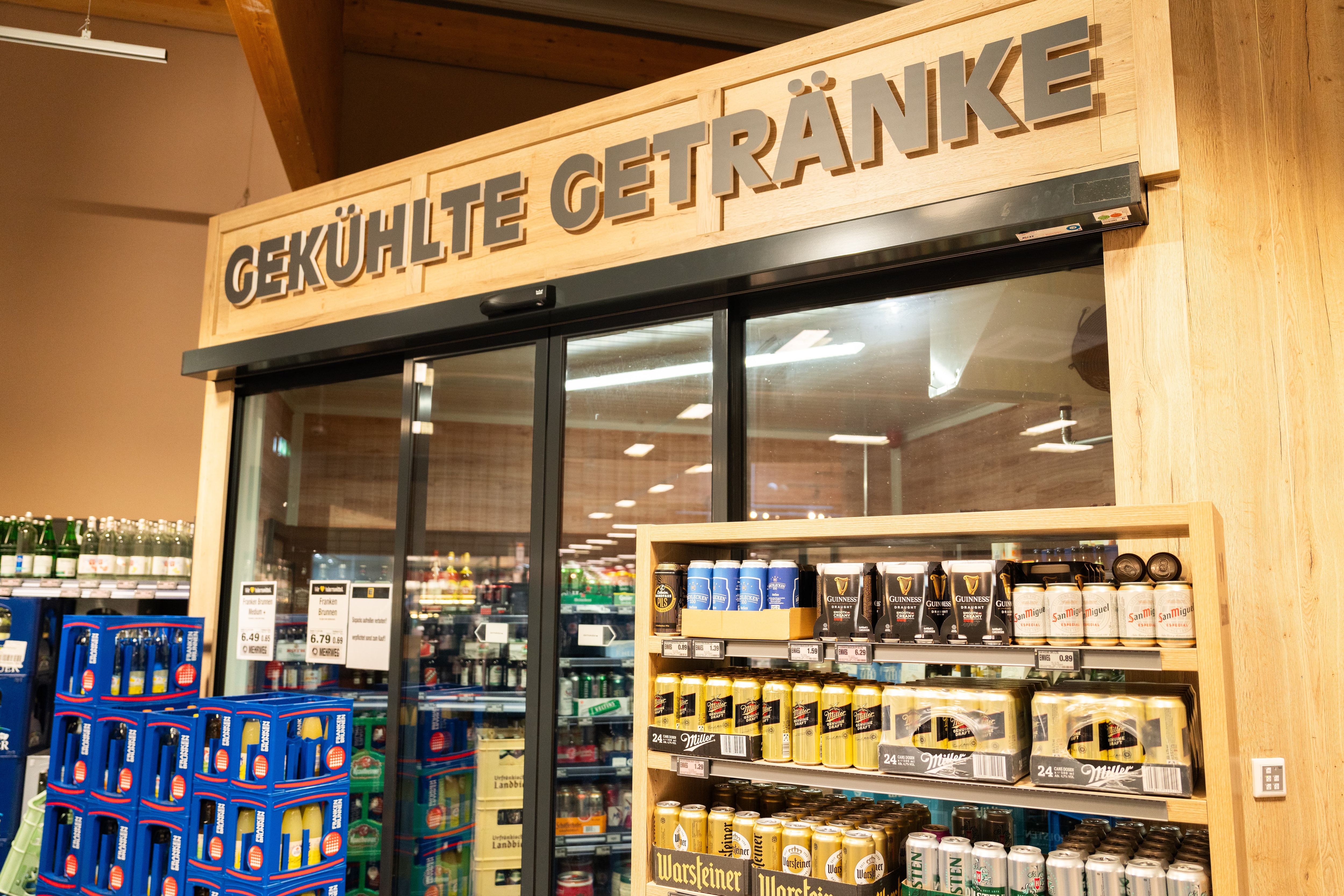 Eingangsbereich mit einer Schiebetür in einer Getränkabteilung eines Edeka-Marktes. Über der Schiebetür steht ein Schriftzug "Gekühlte Getränke".
