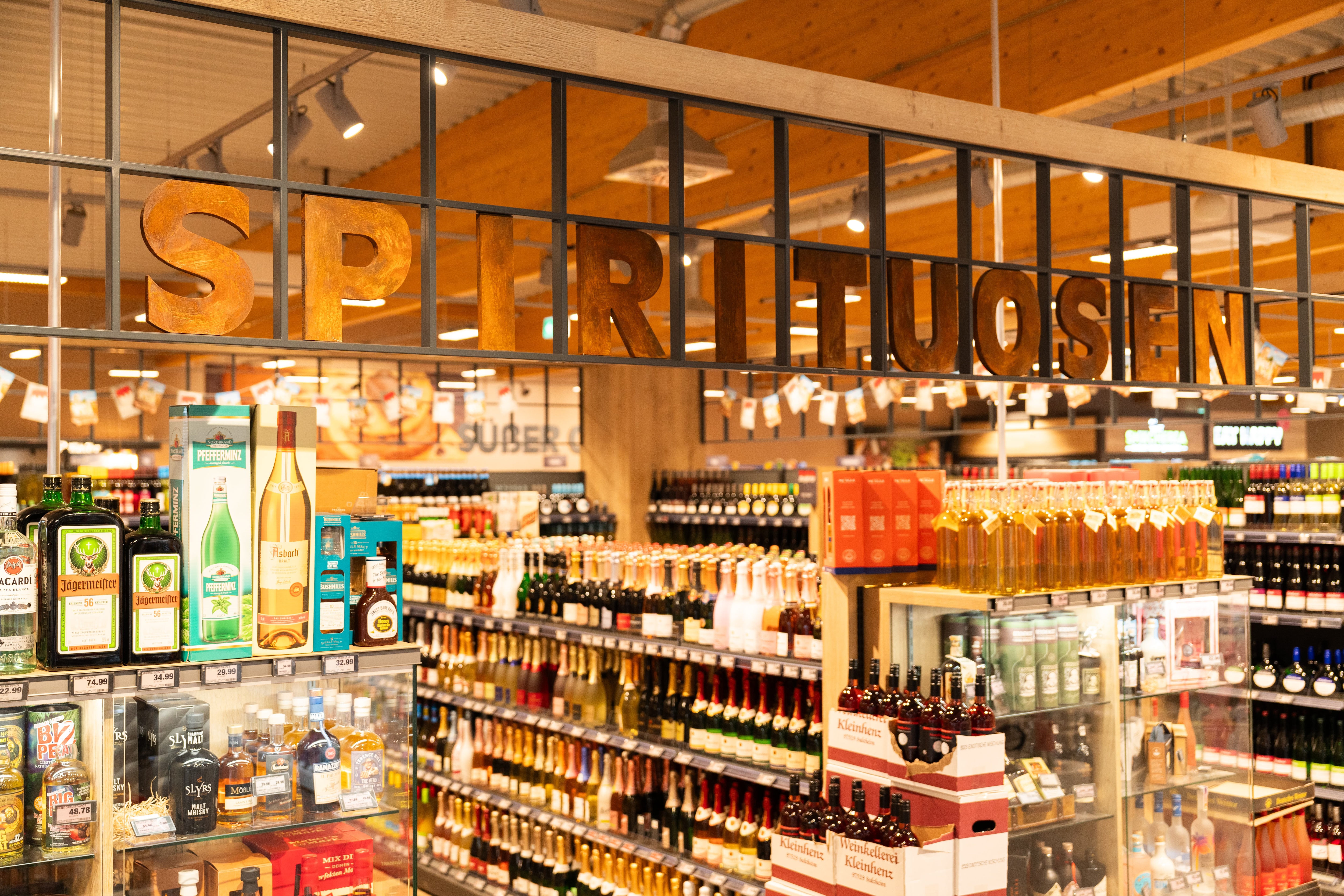 Die Getränkeabteilung eines EDEKA-Markts. Im Hintergrund sind unscharf verschieden Spirituosen zu erkennen. Ein Schriftzug mit "Spirituosen" ist scharf zu sehen.