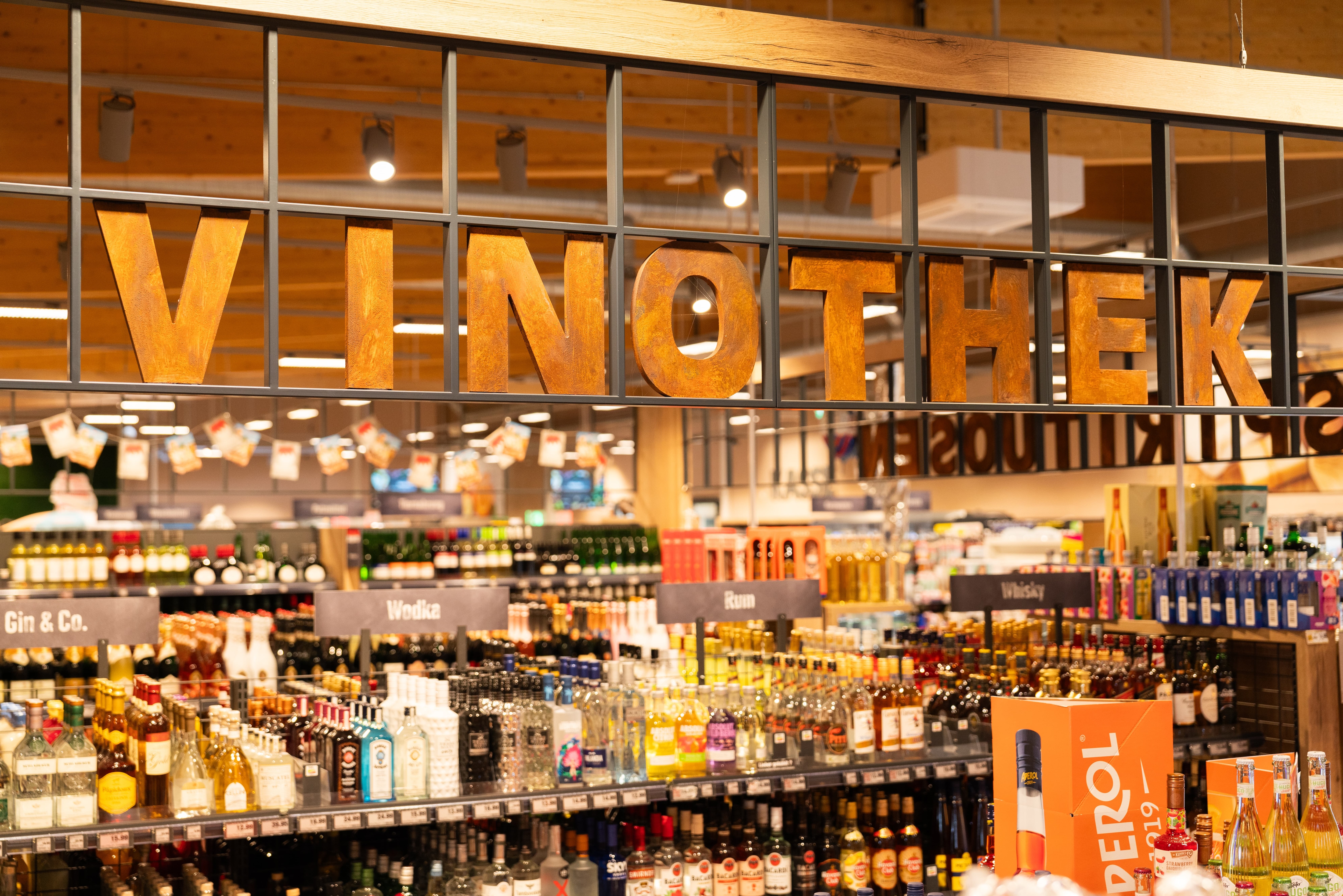 Die Getränkeabteilung eines EDEKA-Markts. Im Hintergrund sind unscharf verschieden Spirituosen zu erkennen. Ein Schriftzug mit "Vinothek" ist scharf zu sehen.