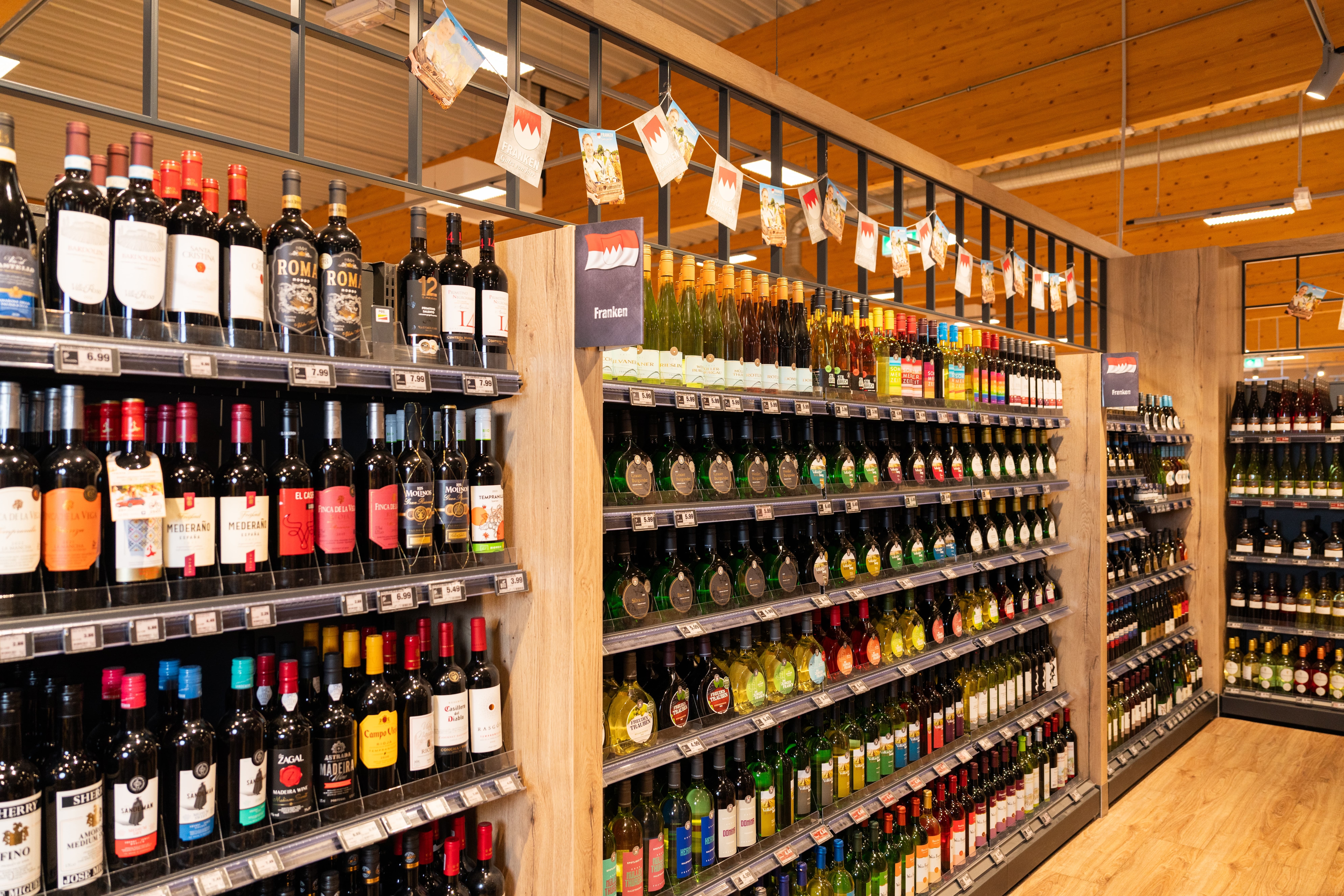 Unterschiedliche Weine stehen aufgereiht in den Regalen in der Weinabteilung eines Edeka-Marktes.