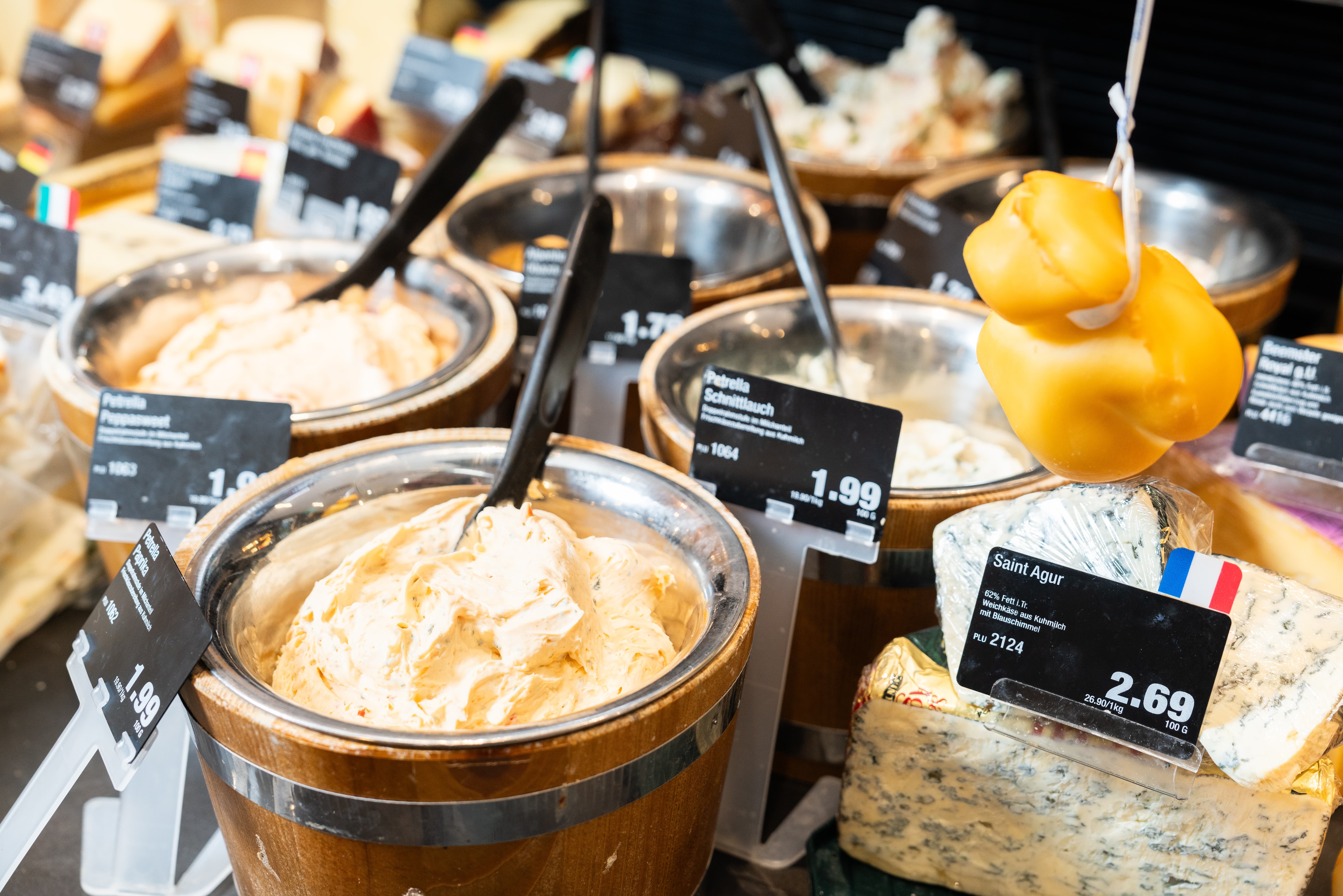 Verschieden kleine Fässer voller Frischkäsespezialitäten in der Auslage einer Käsetheke.