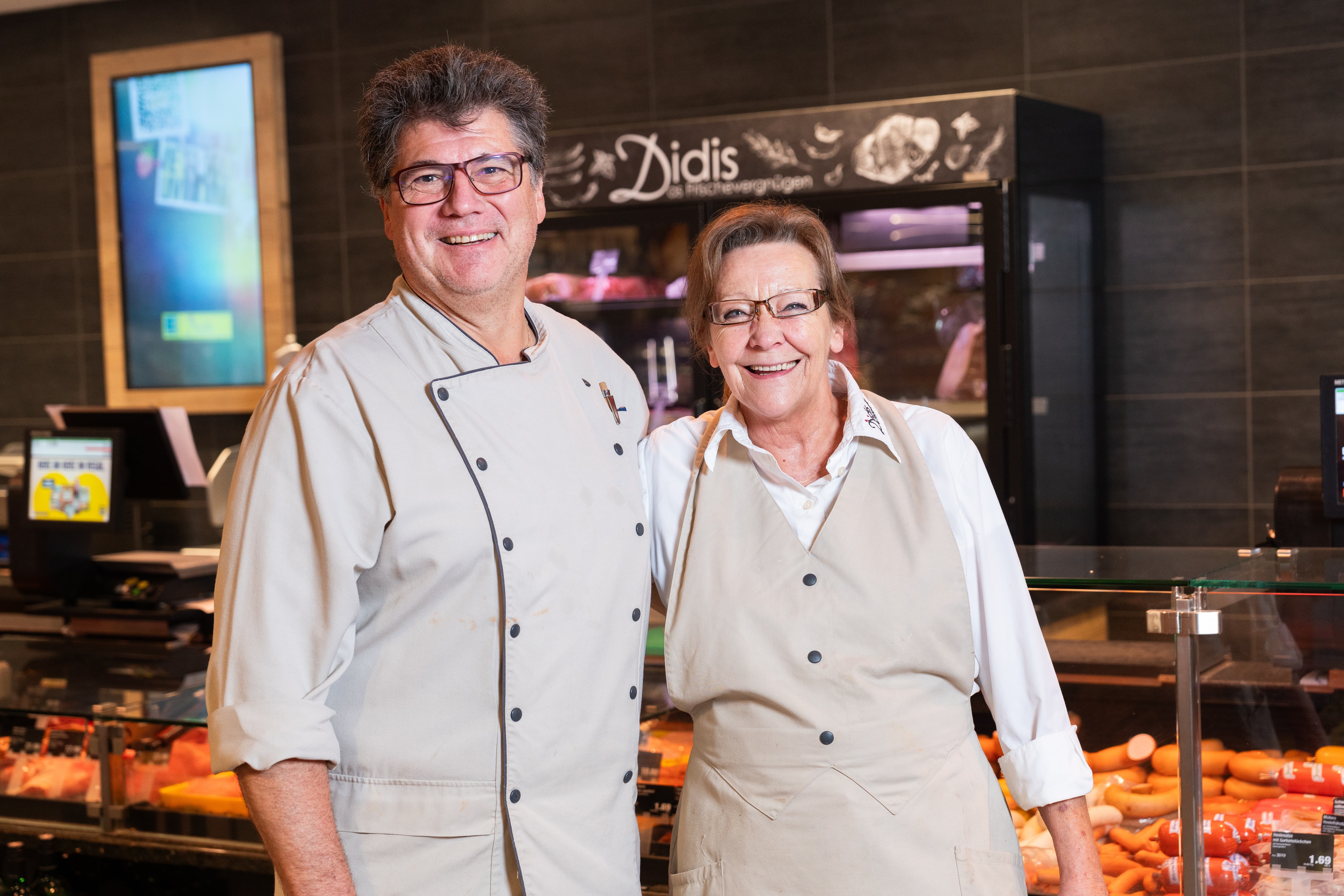 Zwei lächelnde Mitarbeitende eines EDEKA-Marktes vor der Fleischtheke.