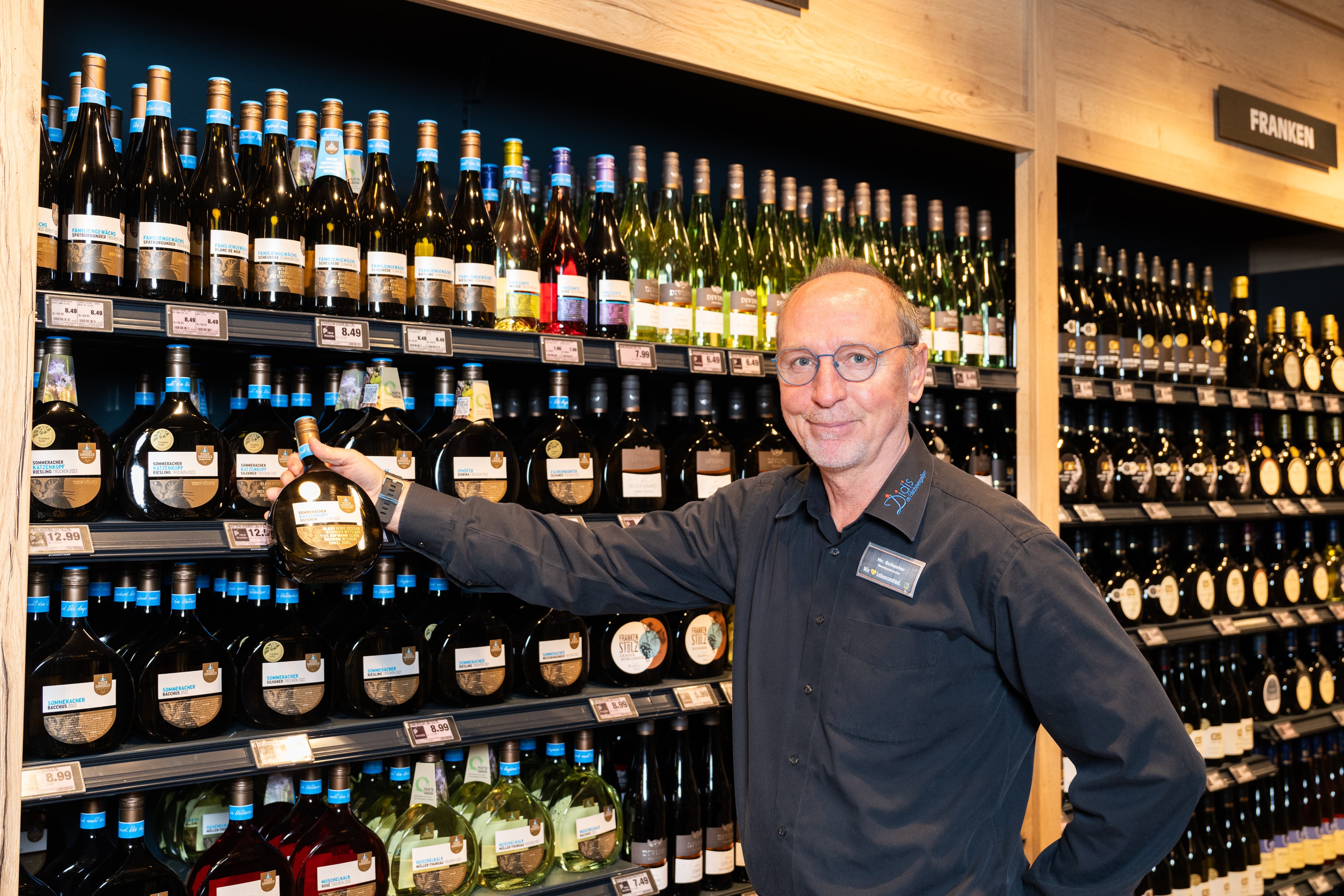 Ein lächelnder Mitarbeiter nimmt eine Flasche Wein aus einem Regal.
