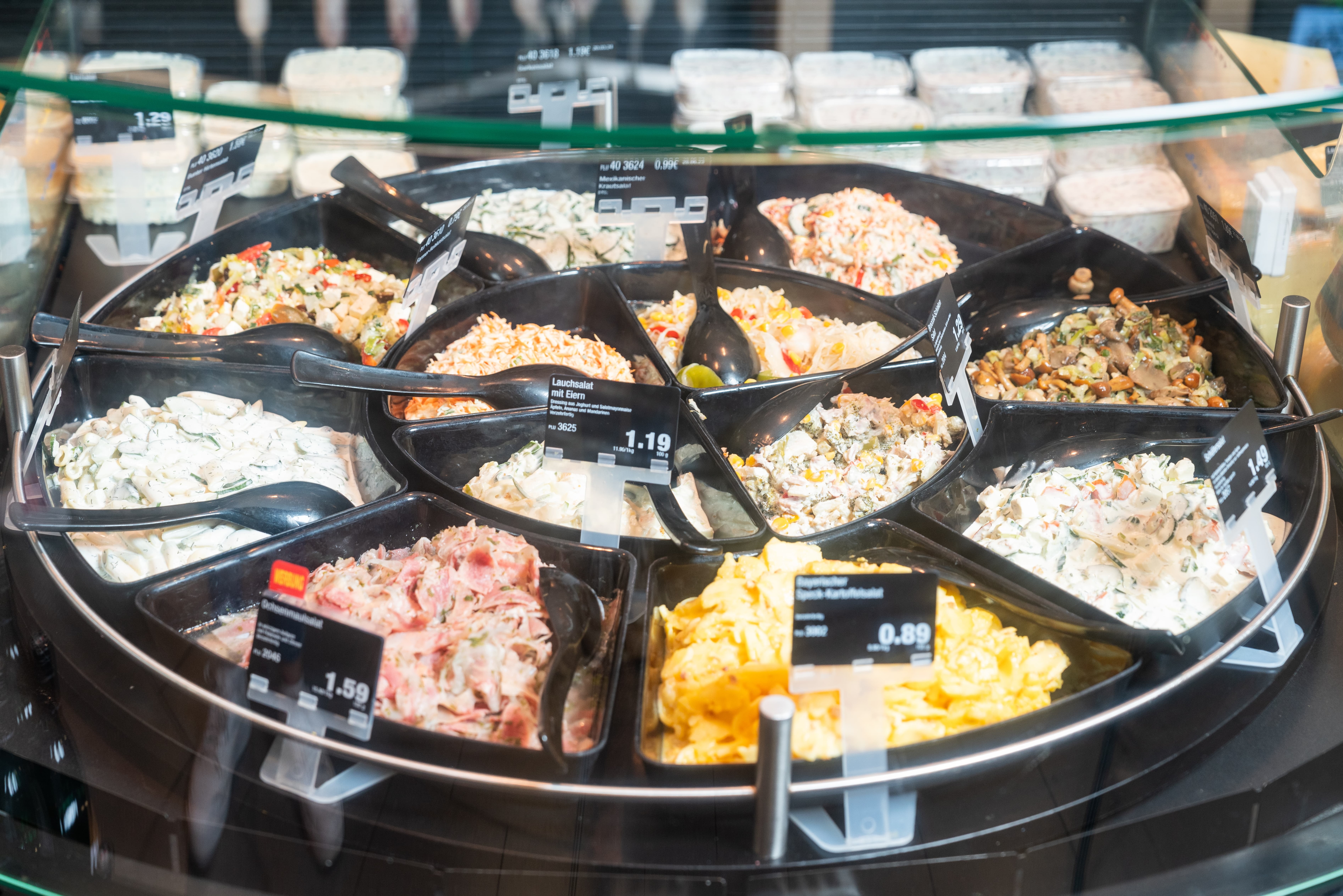 Kreisförmig angeordnete Schalen mit verschiedenen Salaten in der Auslage einer Bedientheke.