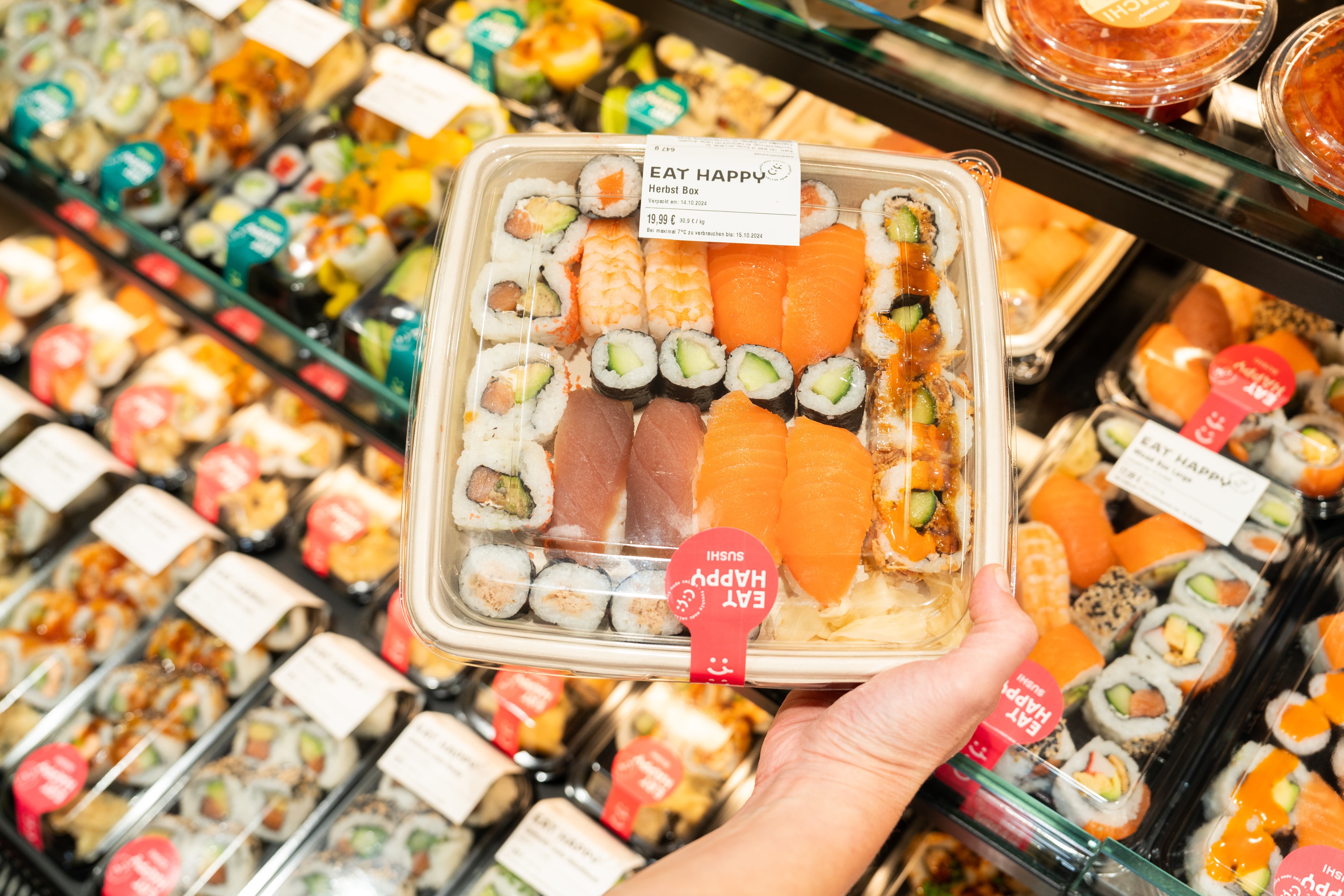 Nahaufnahme einer Hand die eine Packung mit frischem Sushi hält.