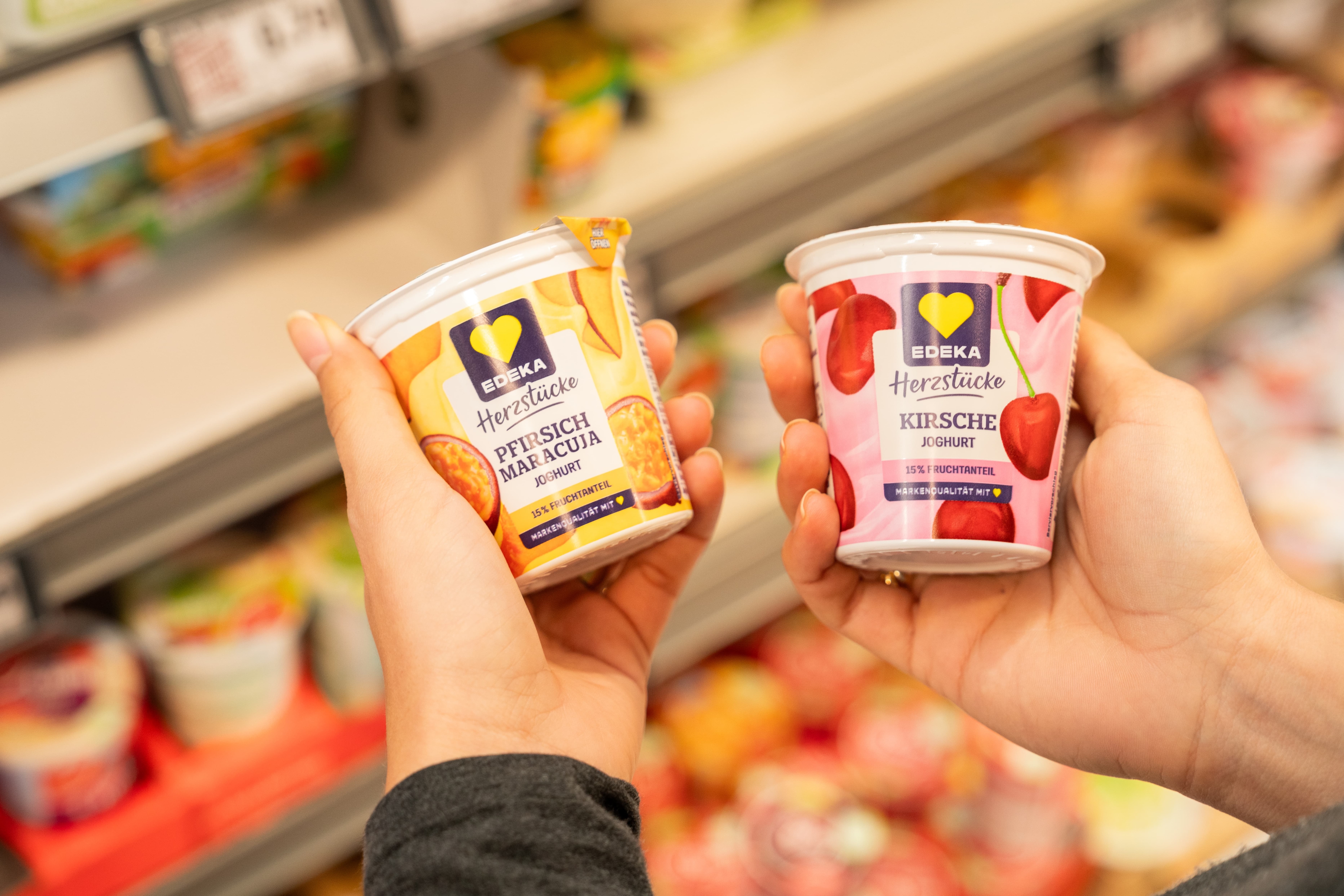Nahaufnahme zweier Hände die jeweils eine Joghurtsorte der EDEKA-Eigenmarke "Herzstücke" halten.