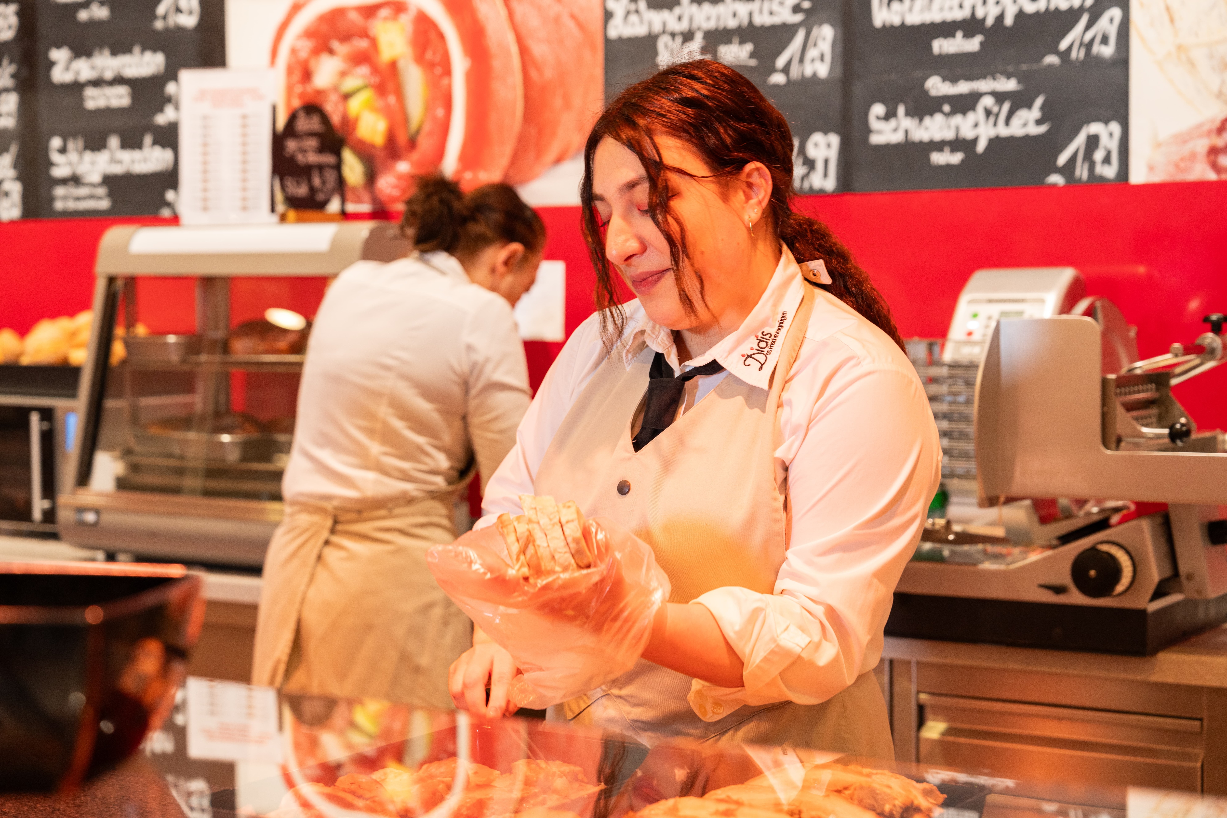 Eine lächelnde Mitarbeiterin packt Fleischprodukte in eine Plastiktüte.